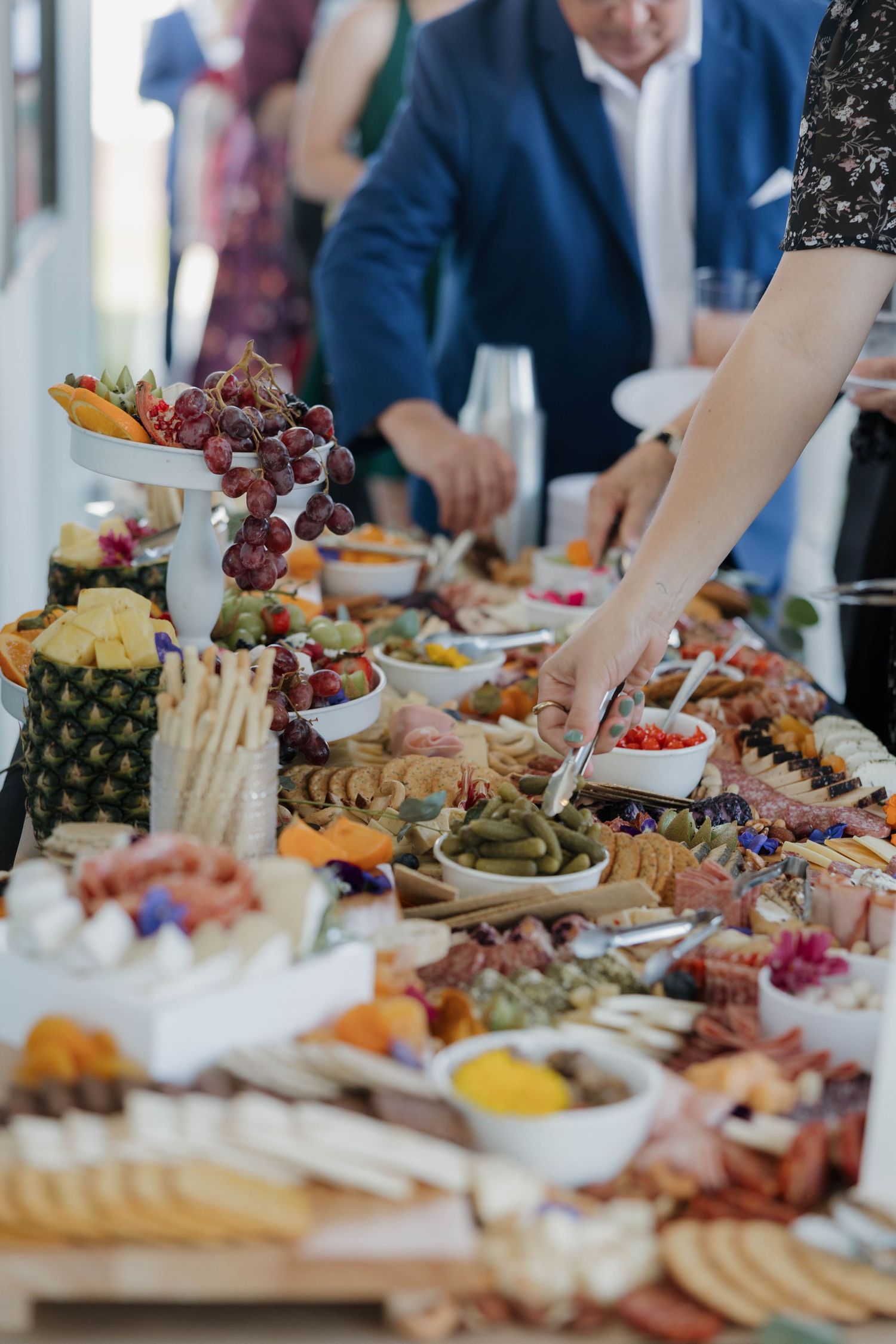 Elegant charcuterie and appetizer spread at an upscale event with fresh fruits, meats, and cheeses being served.