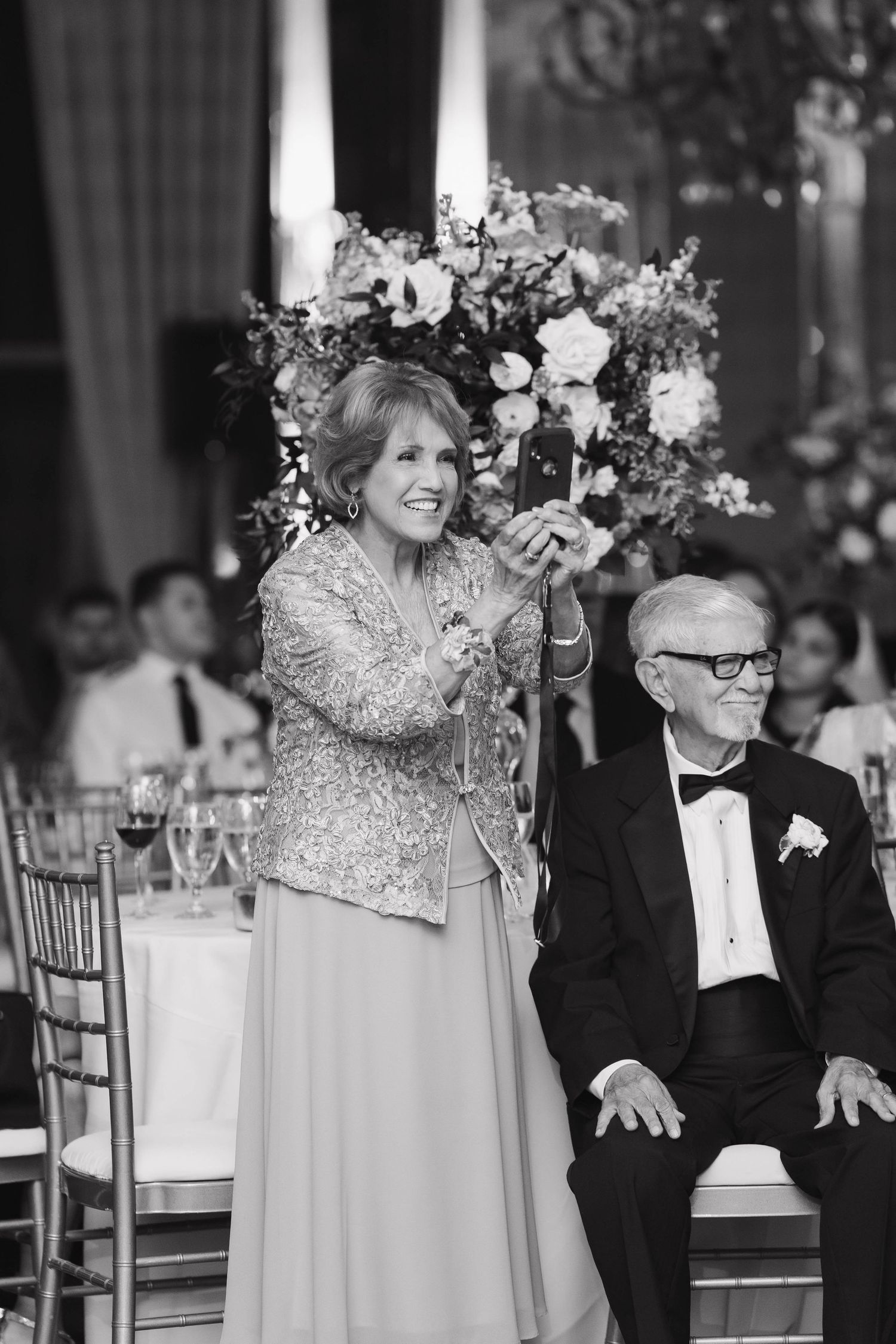 Wedding guests in formal attire react with joy during reception celebrations.