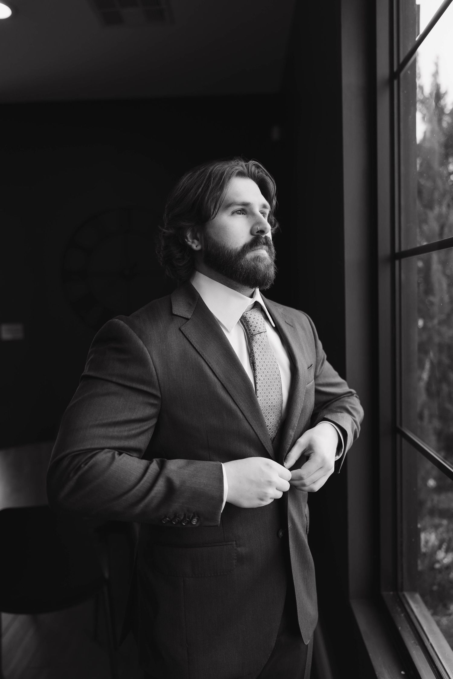 Professional black and white photo series showing a man in a suit adjusting his tie while looking out a window.