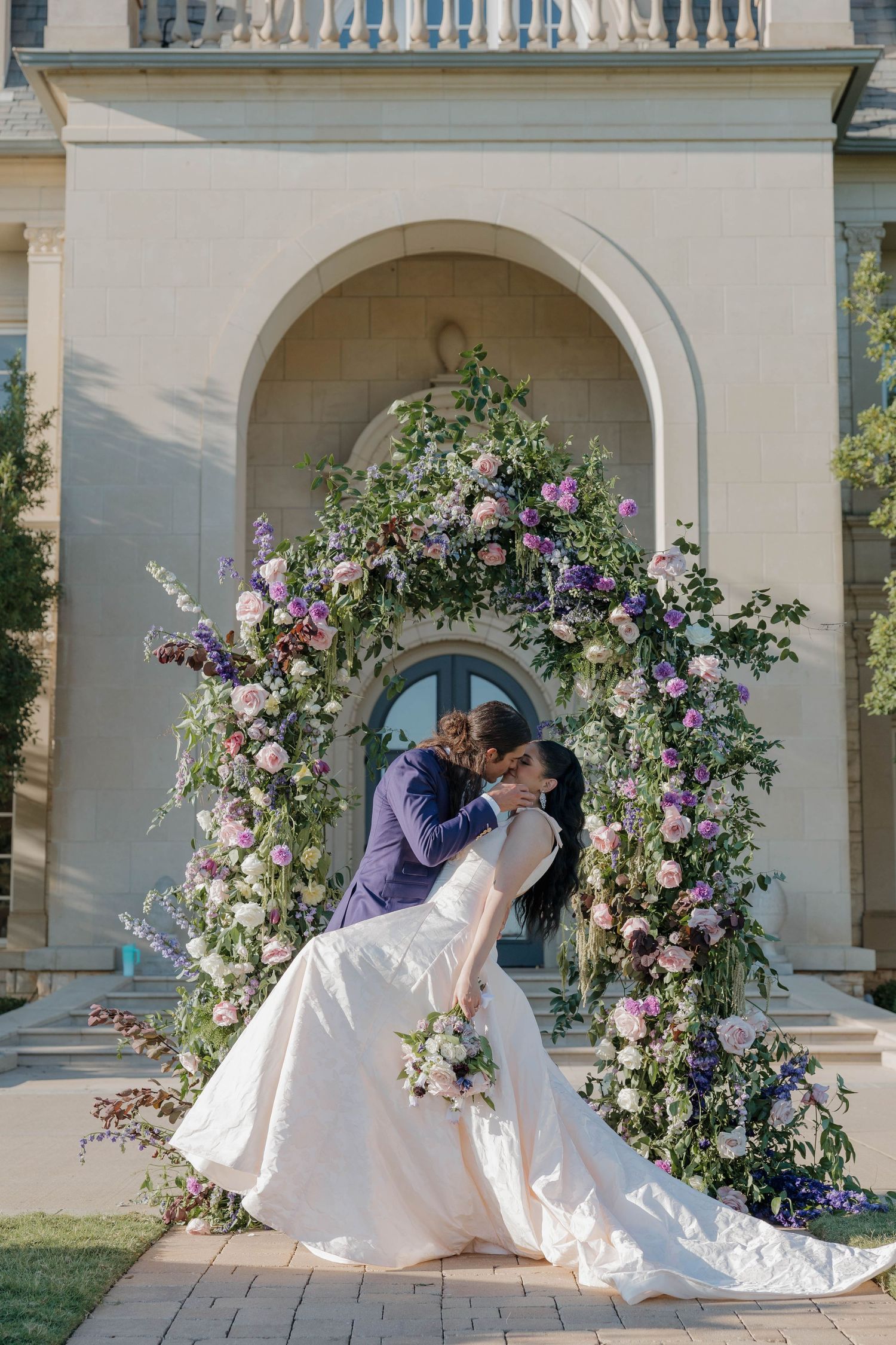 Three romantic wedding photos show a couple in an elegant embrace under beautiful floral arches at a grand venue.