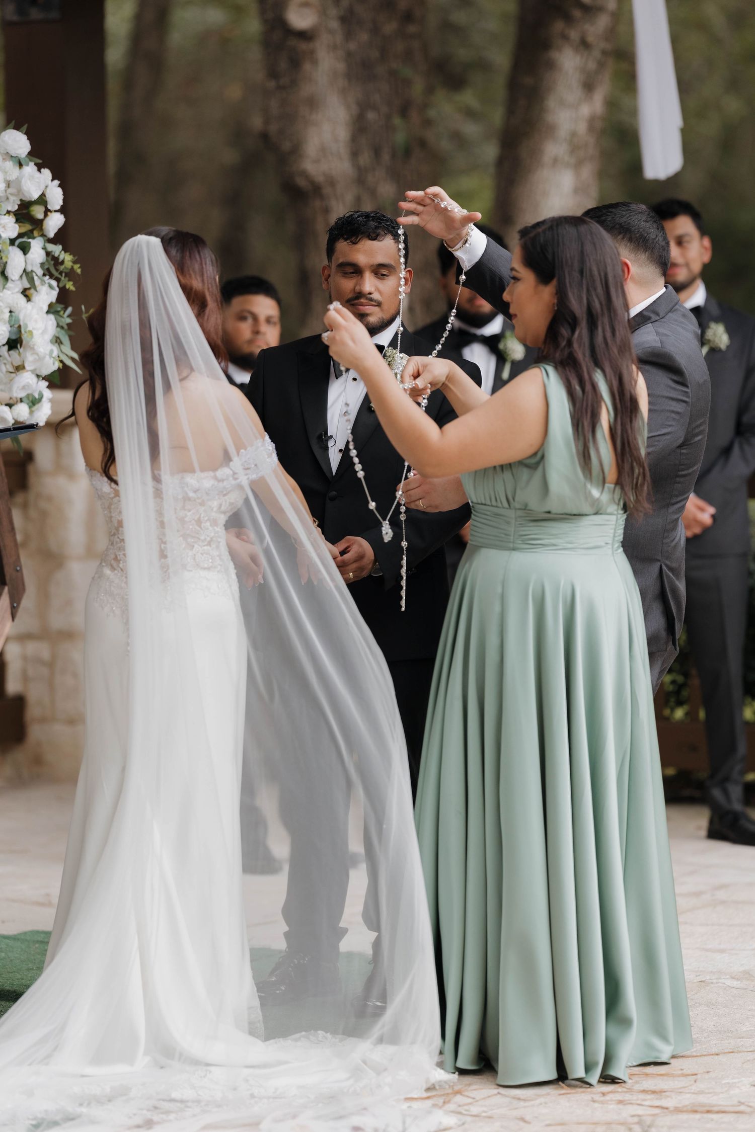 Bridesmaids in sage green dresses and bride in white gown dancing together at outdoor wedding celebration.