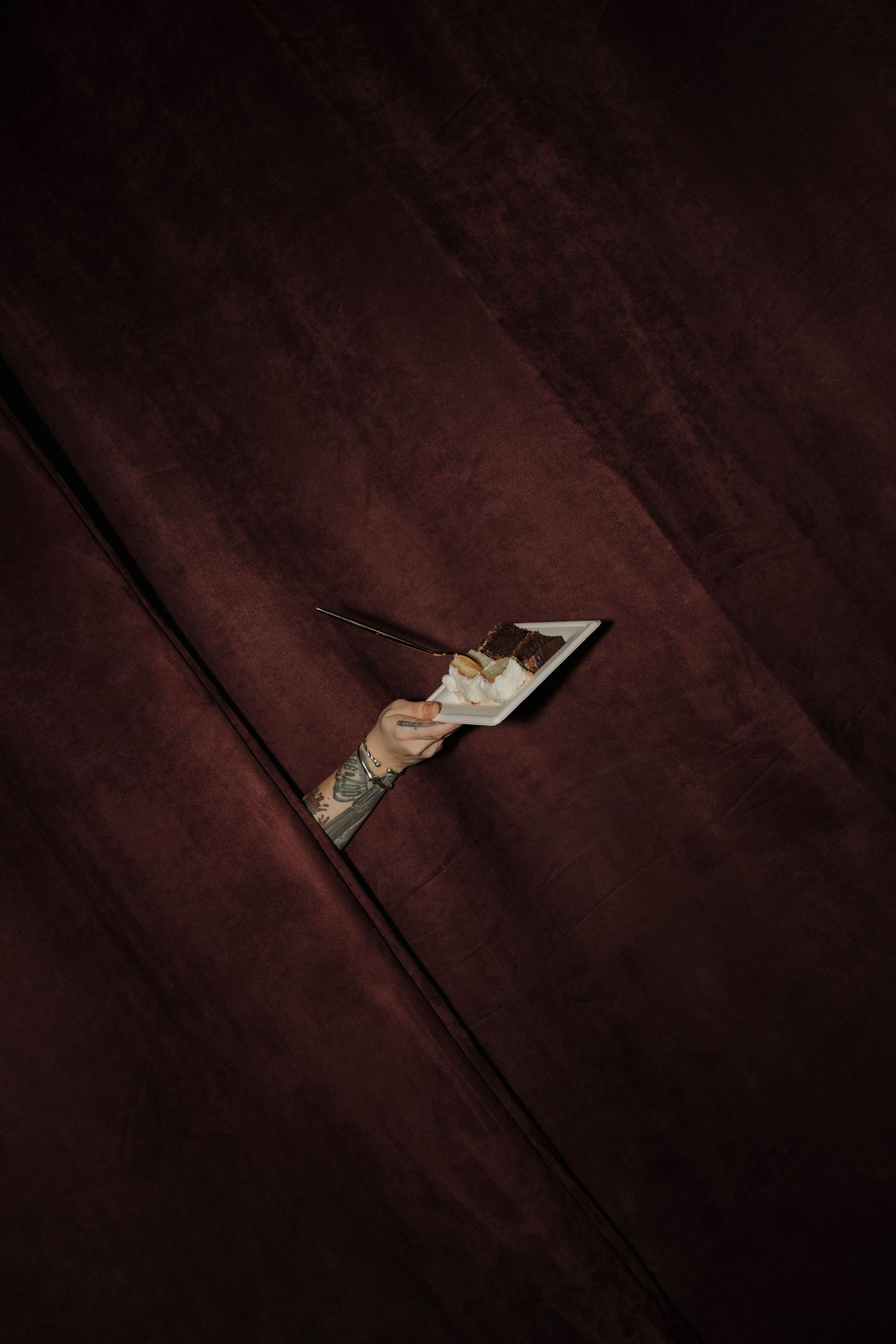 A close-up photo of a playing card peeking through dark burgundy velvet curtains or fabric.