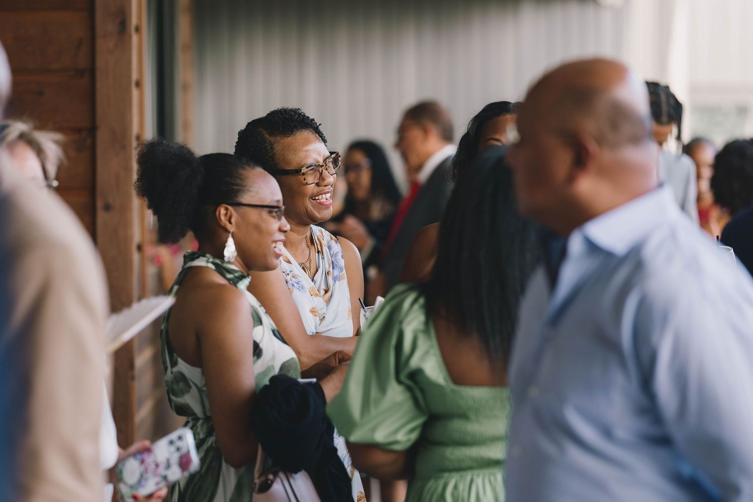 Wedding guests in formal attire smile and socialize during a reception gathering.