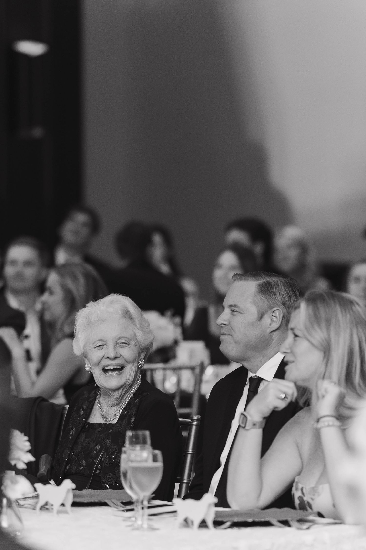 Black and white photo showing guests laughing and enjoying themselves at a formal dinner event.