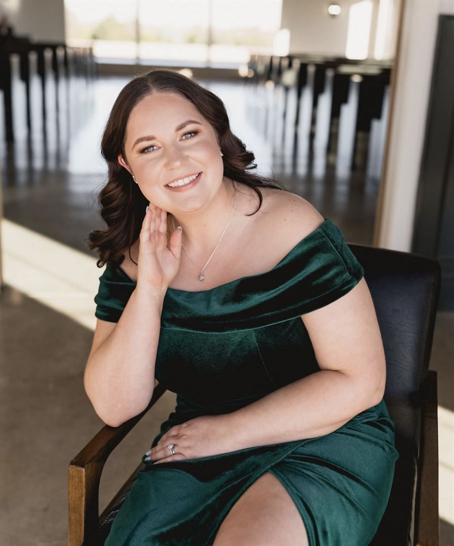 A person in an elegant emerald green velvet dress poses gracefully in an indoor setting.