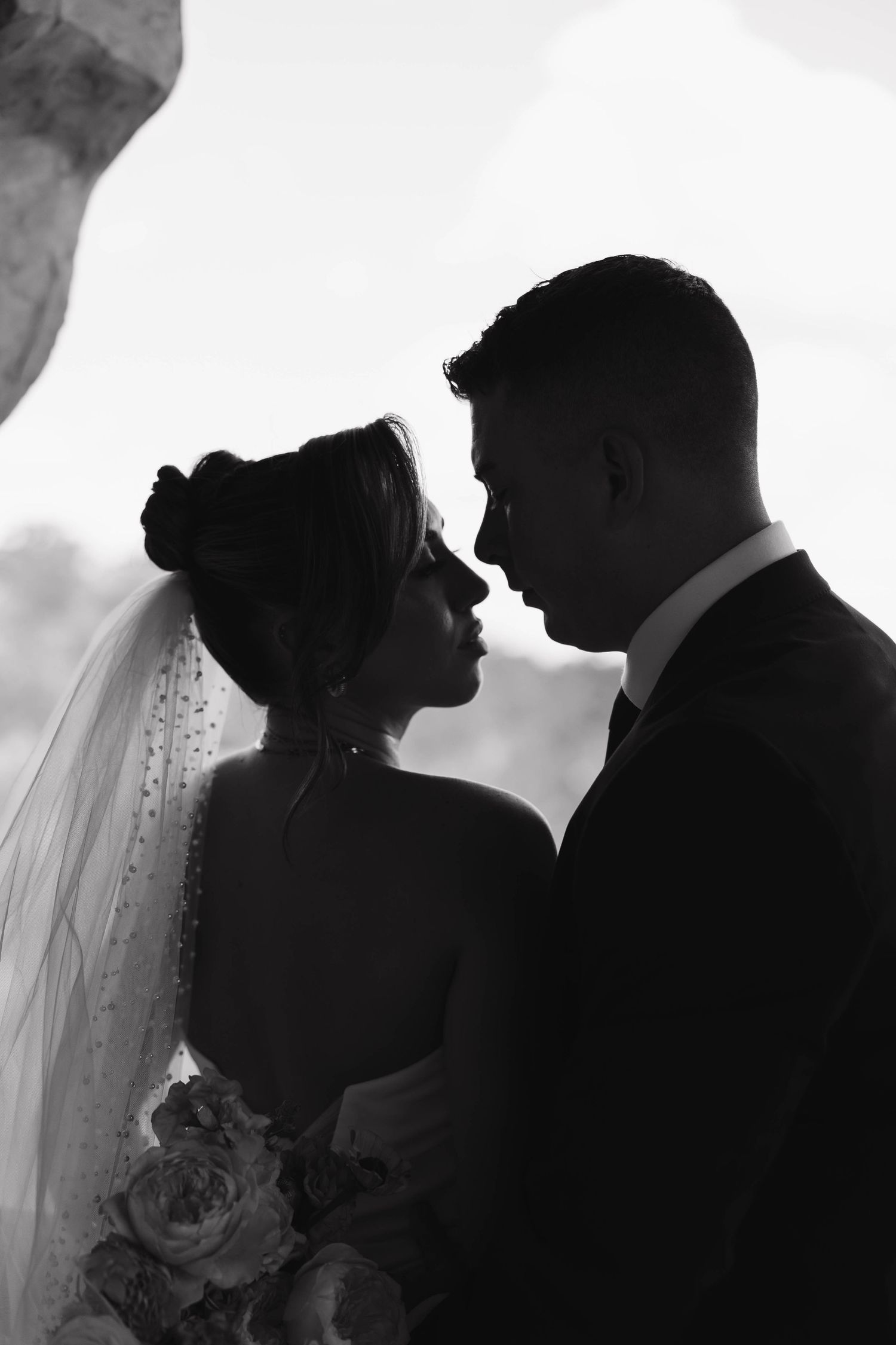 A romantic black and white silhouette of a bride and groom about to kiss, with wedding veil and bouquet details visible.