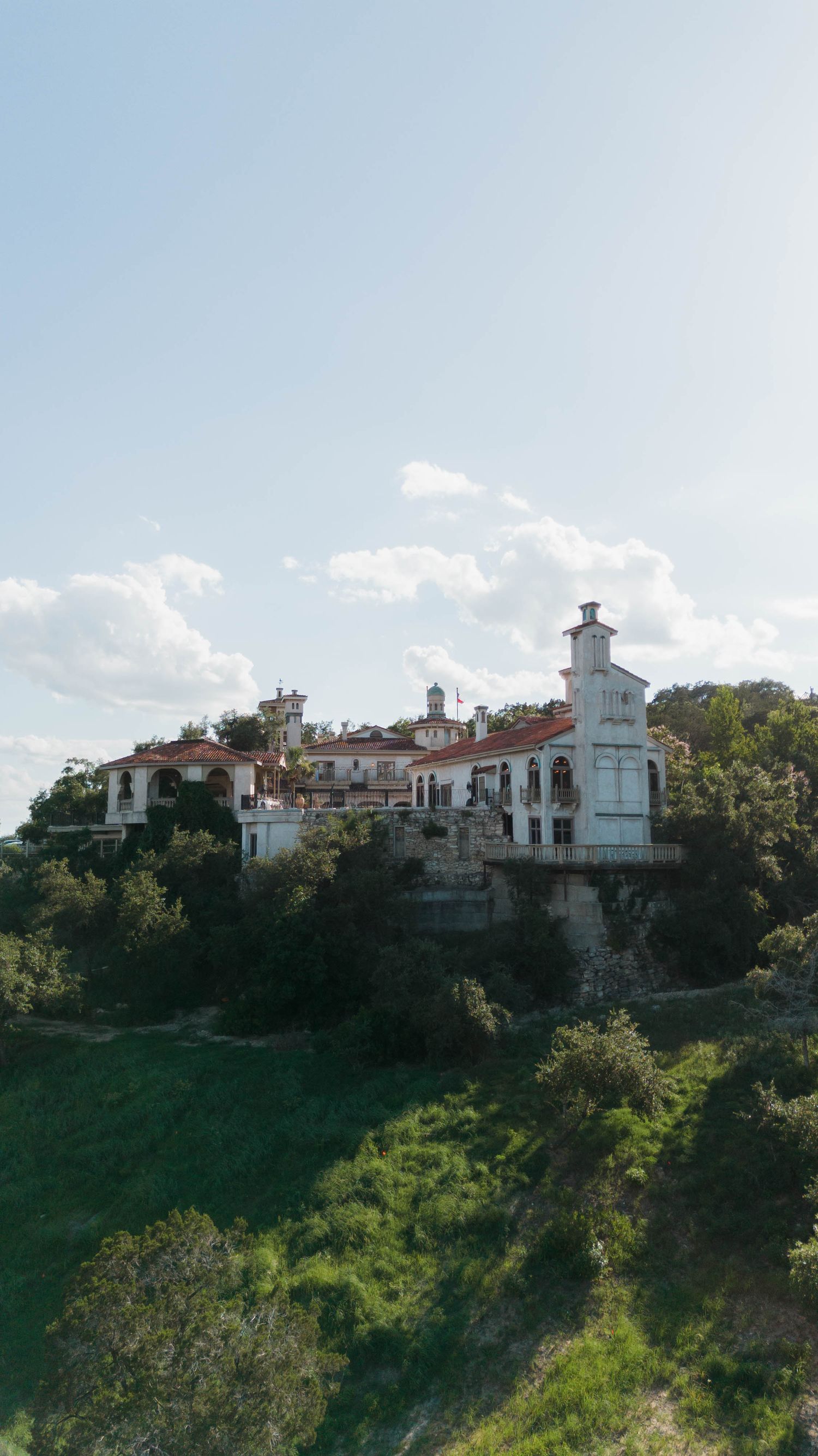 White Mediterranean villa perched on a hillside with red tile roofs against blue sky.