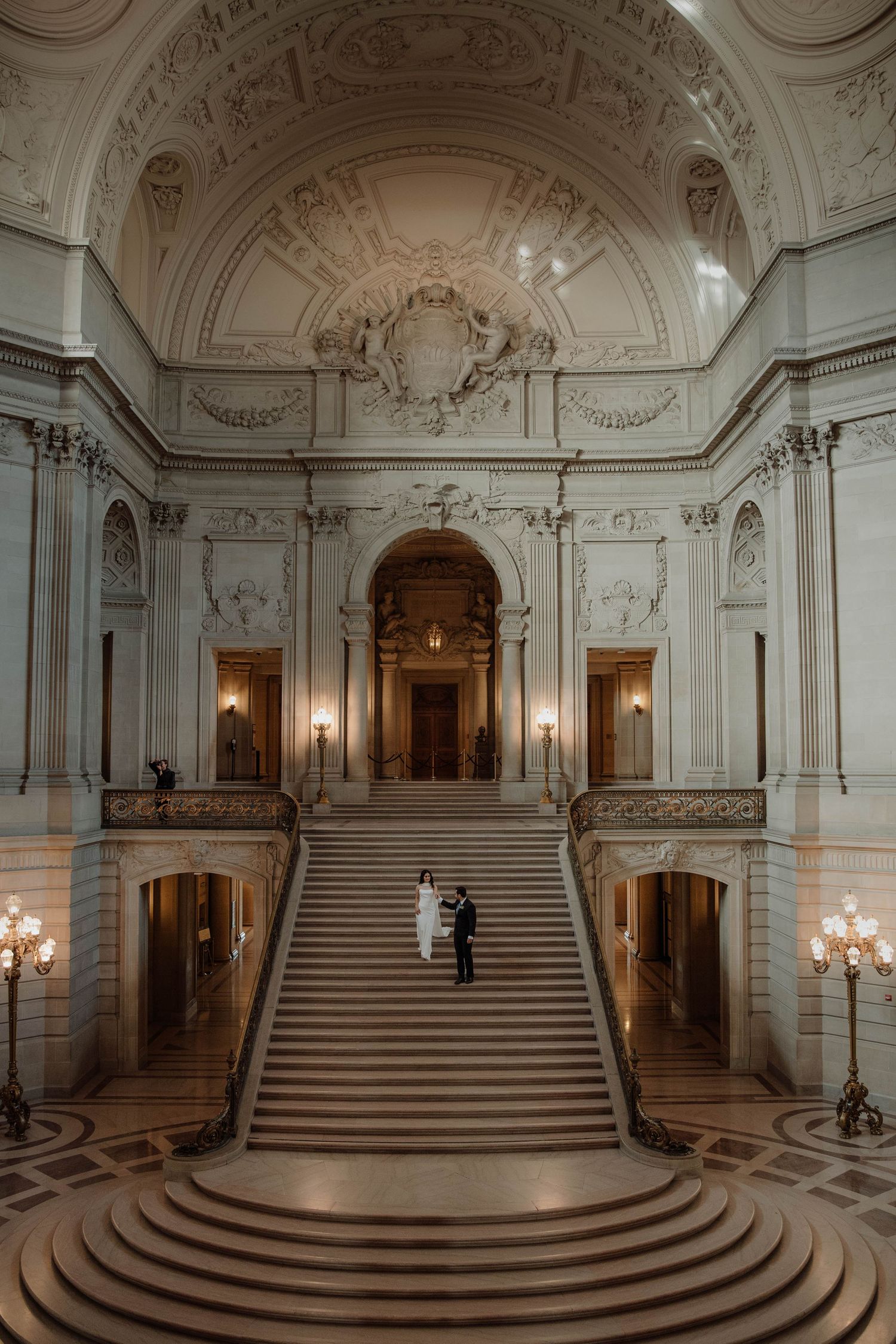 Panoramic view of an ornate Baroque palace interior with grand marble staircases and crystal chandeliers.