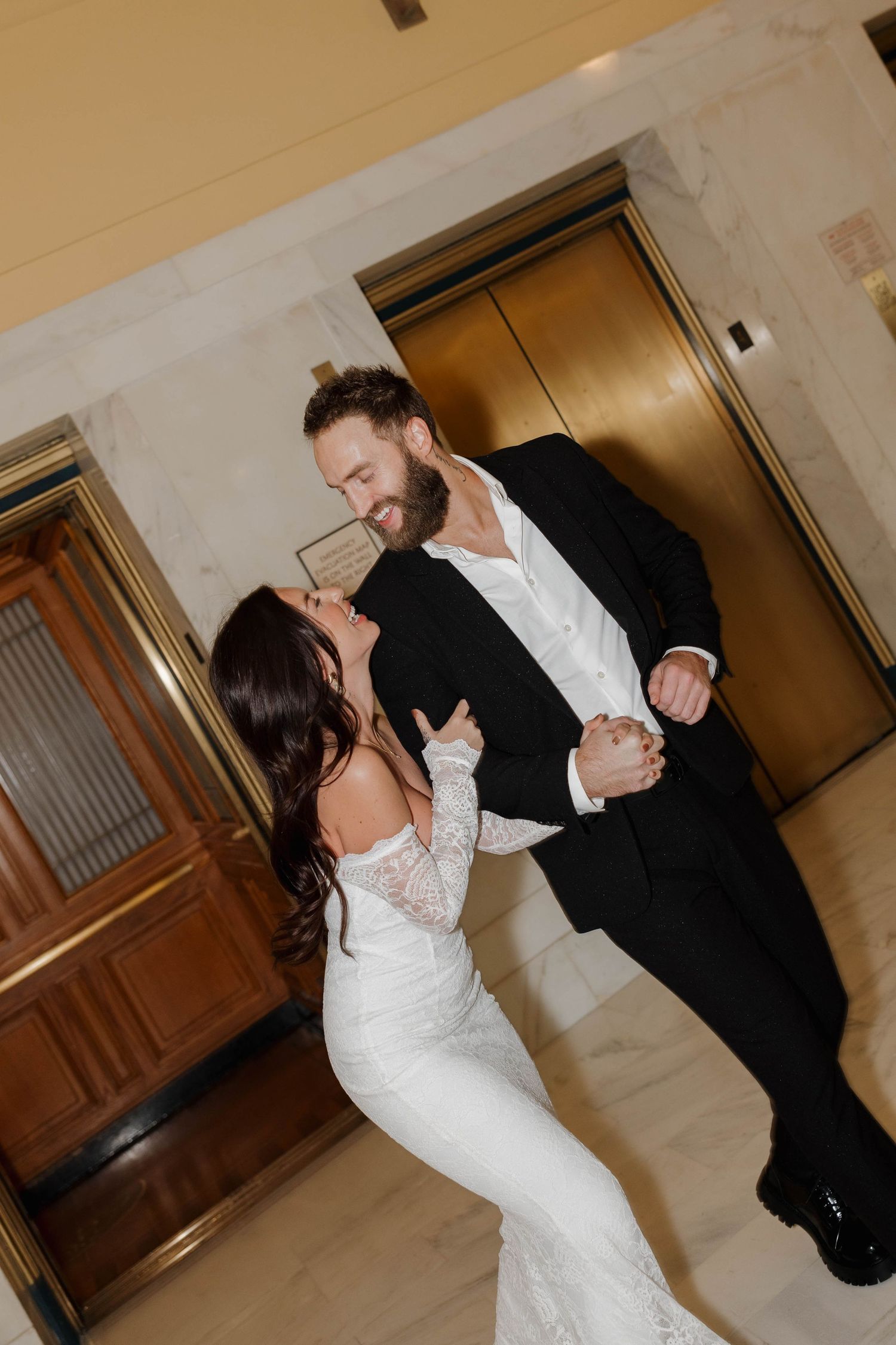 A romantic couple dancing together at a wedding, with the bride wearing a white lace gown and the groom in a black suit.