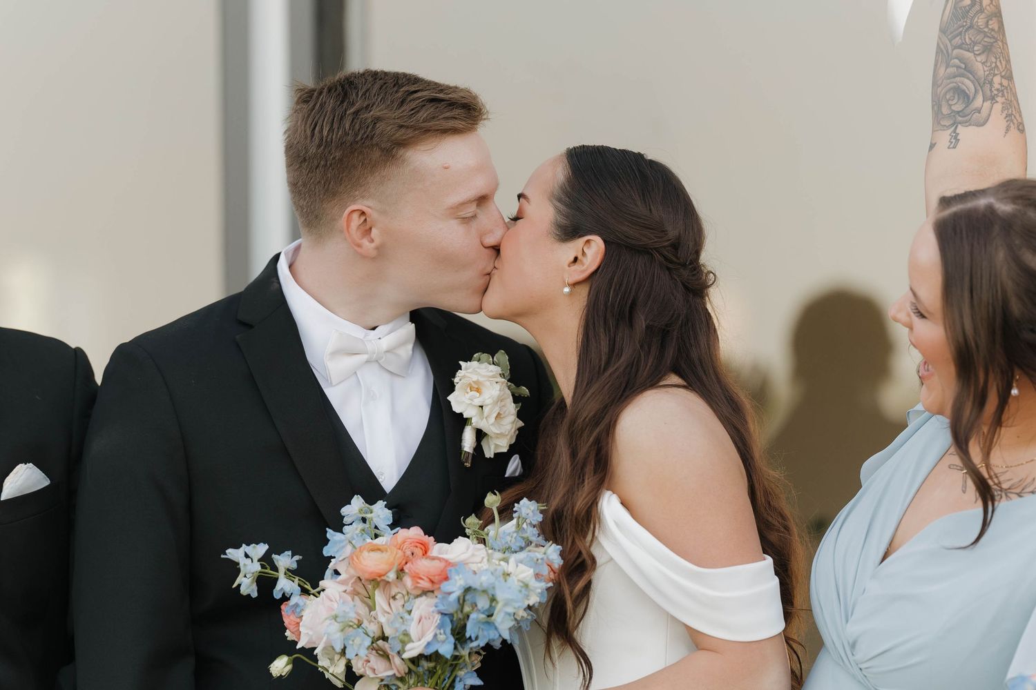 A romantic wedding moment with the bride holding a pastel bouquet of blue and peach flowers at an indoor venue.