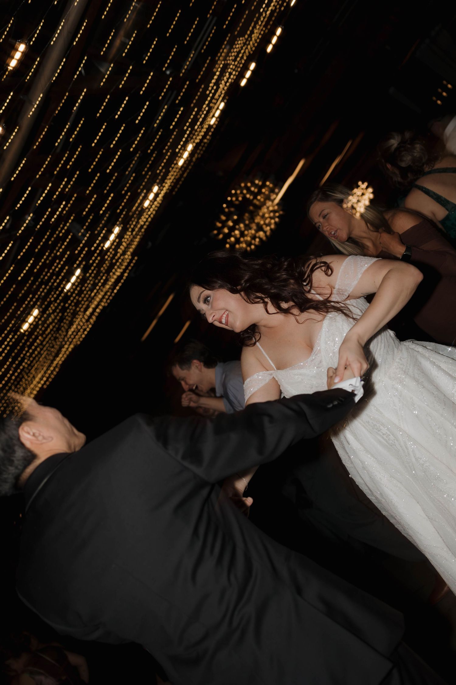 Wedding reception candid moment captured with dramatic lighting and string light decorations.