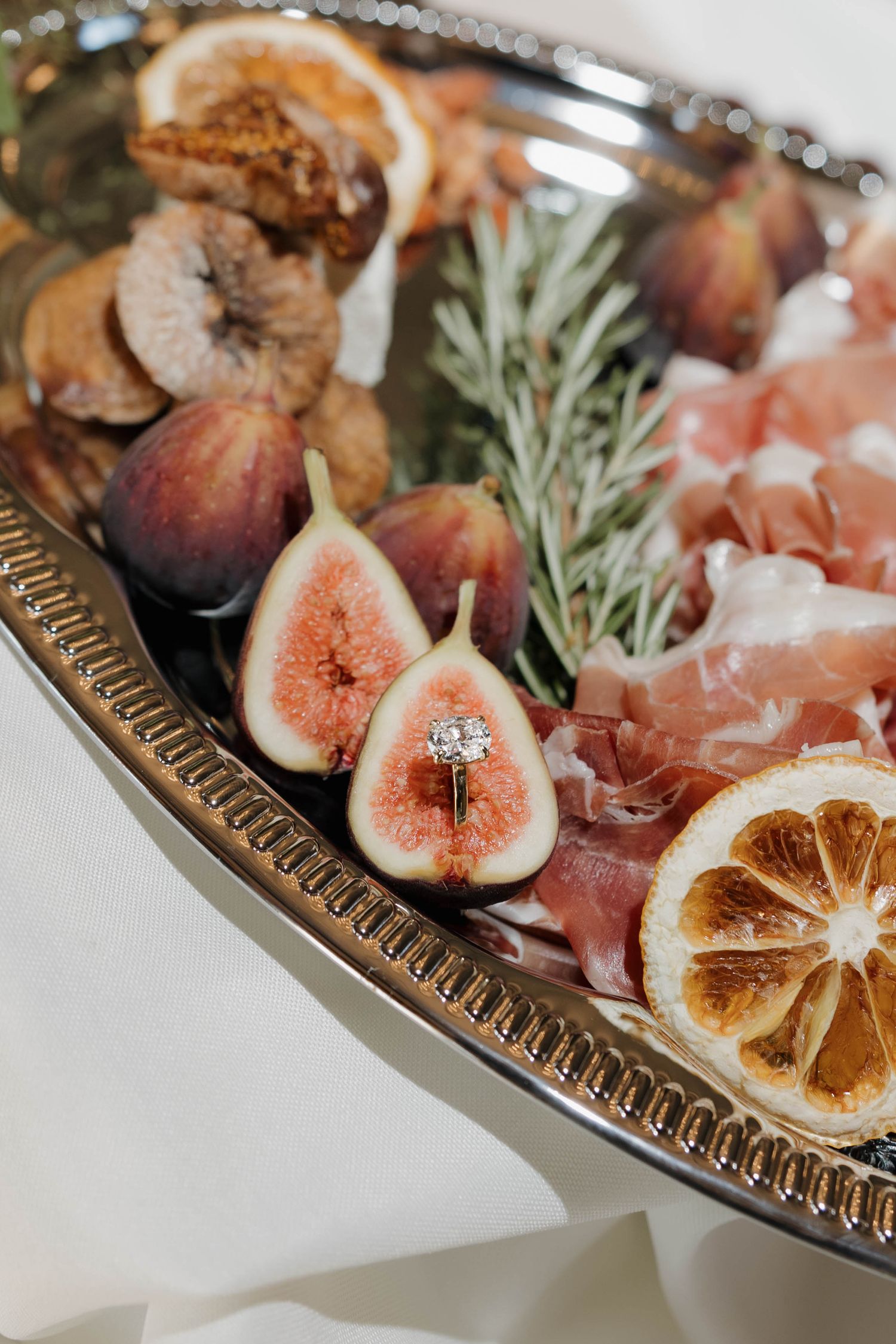 Fresh figs, prosciutto, and dried citrus slices arranged elegantly on a decorative silver serving platter.