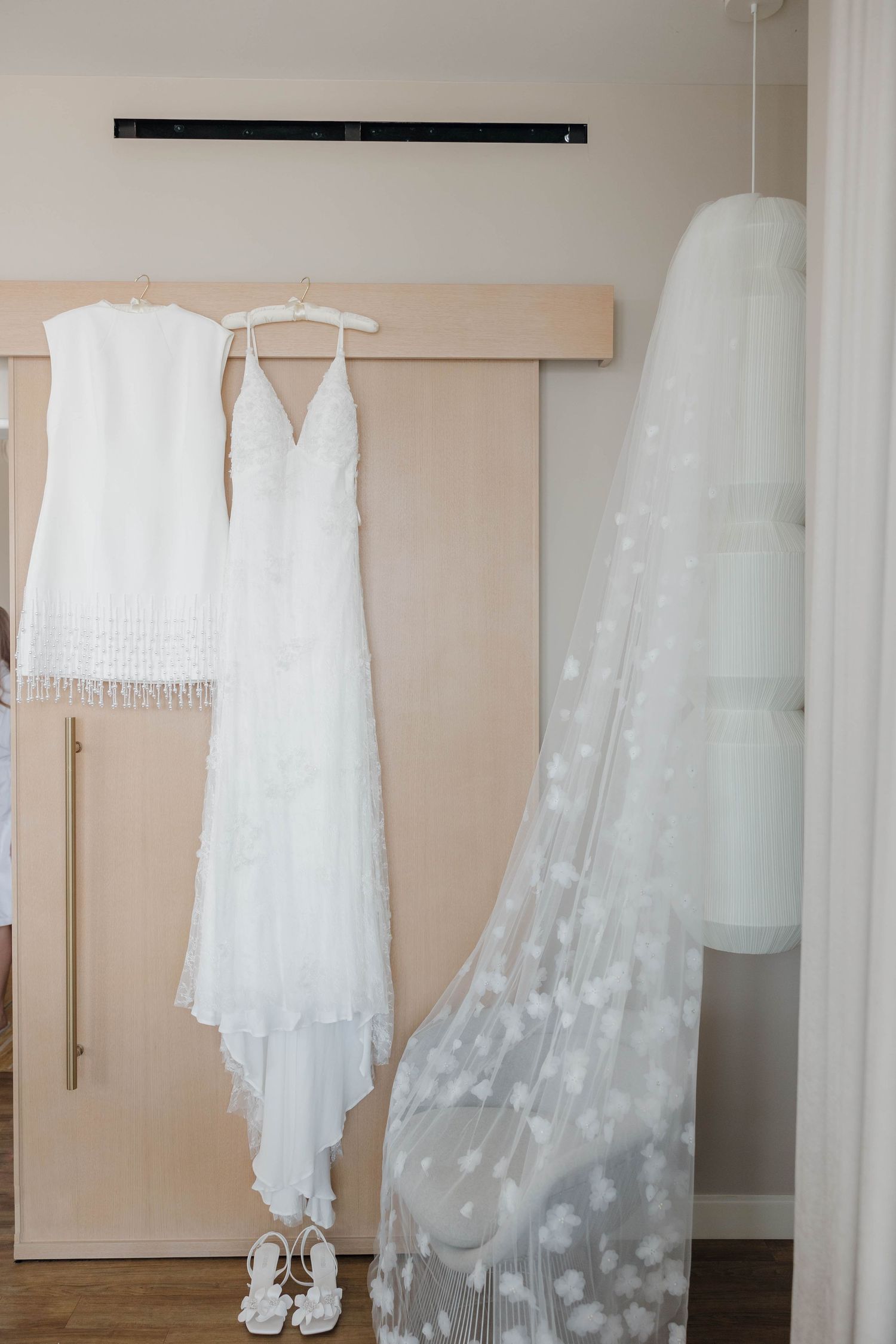 Wedding dresses and veils hanging on display against a beige wall in a bridal boutique.