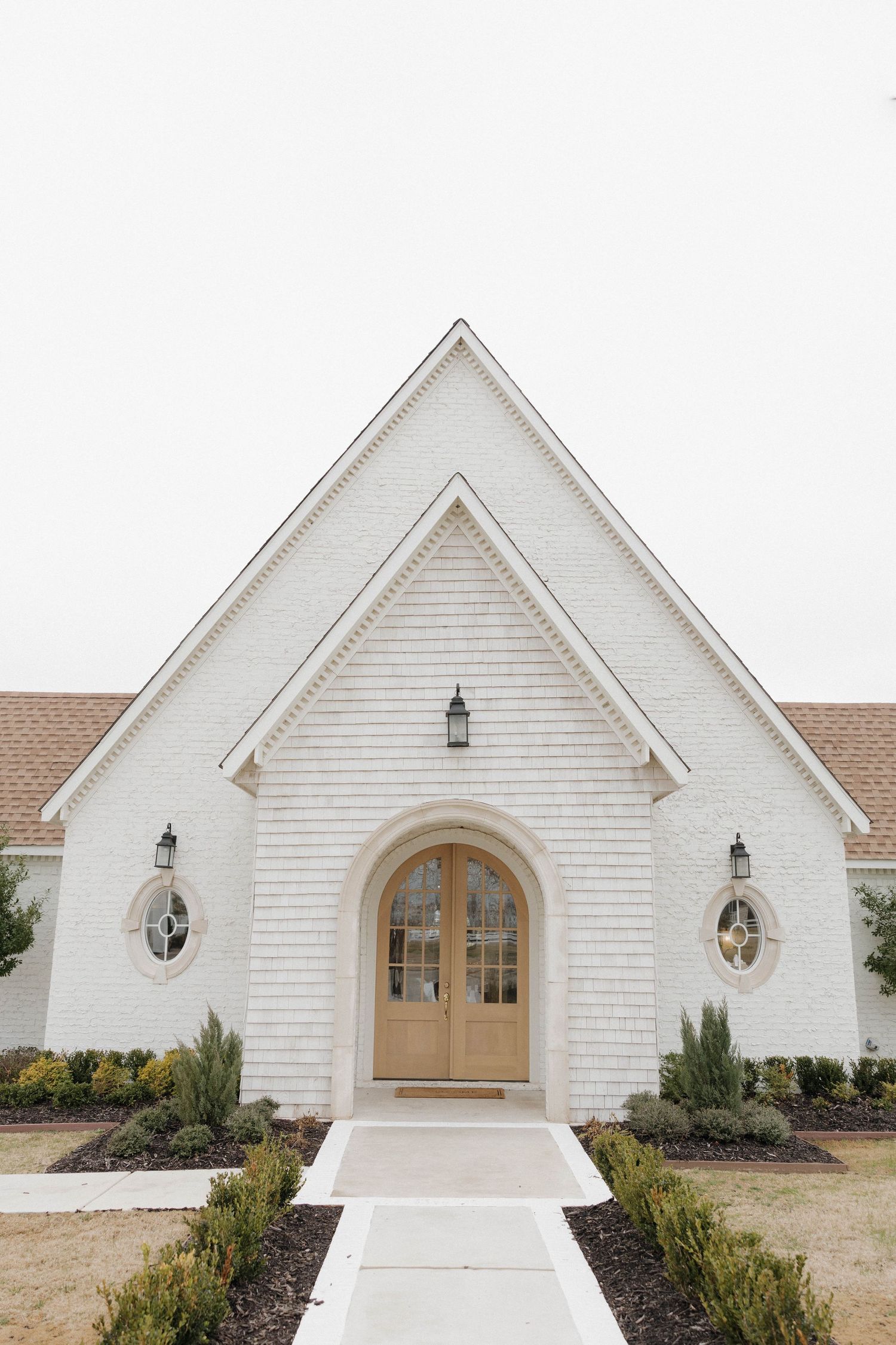 White church facade with wooden double doors and arched entryway adorned with lantern-style sconces.