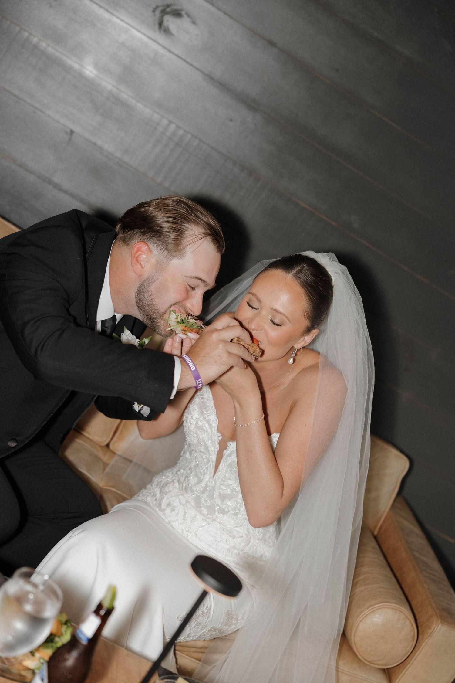 A newlywed couple shares a playful moment while eating cake together at their wedding reception.