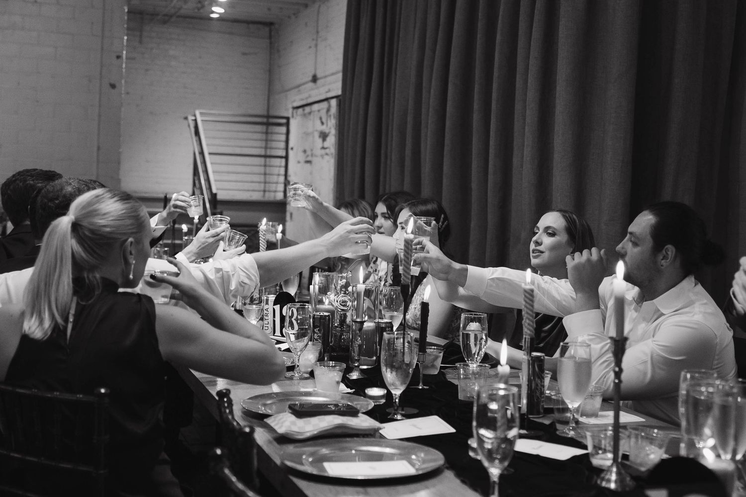 A group at a dinner party raises glasses in a toast, captured in black and white at a restaurant table.
