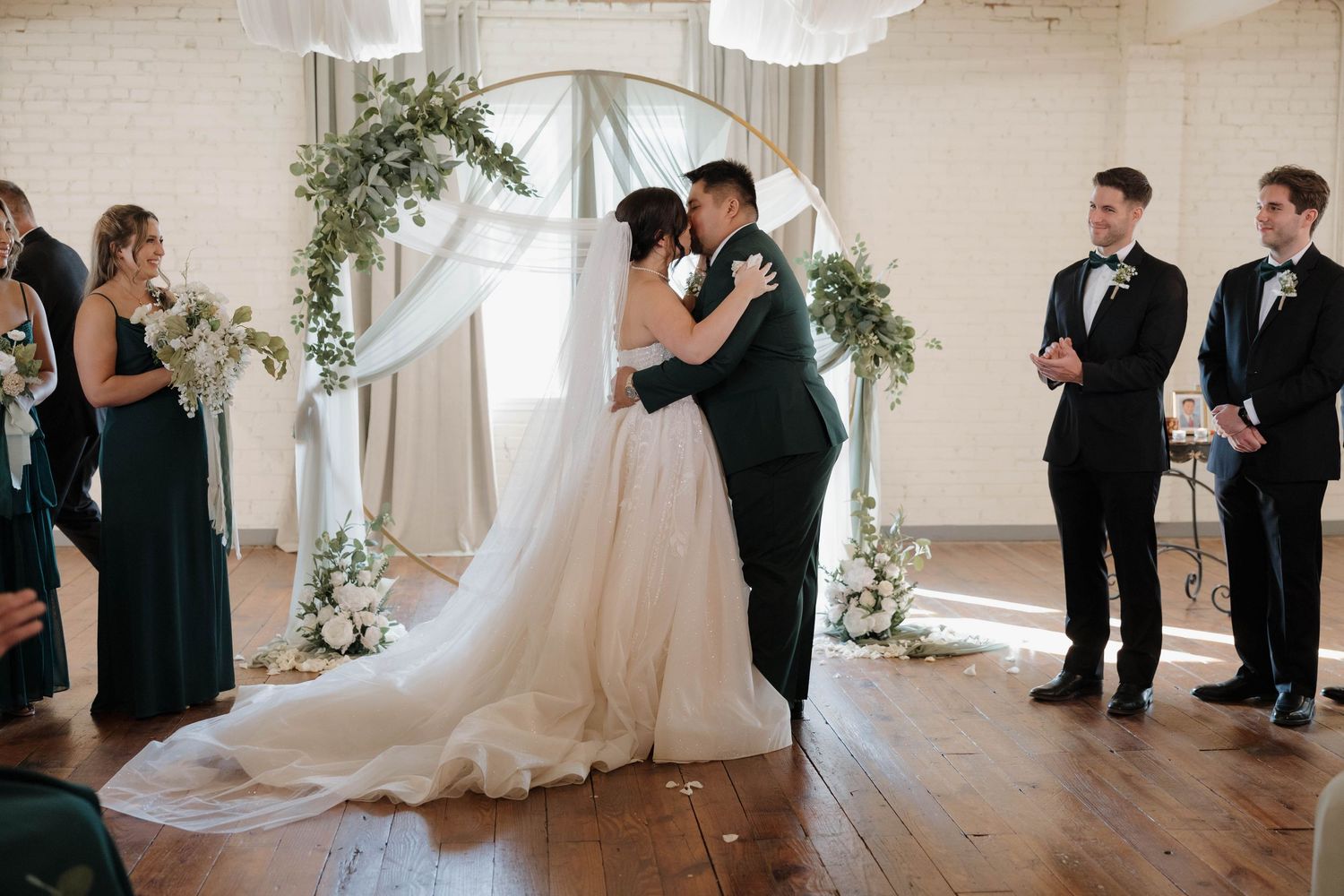 A bride in a flowing white gown walks down a bright indoor aisle at an elegant wedding ceremony.