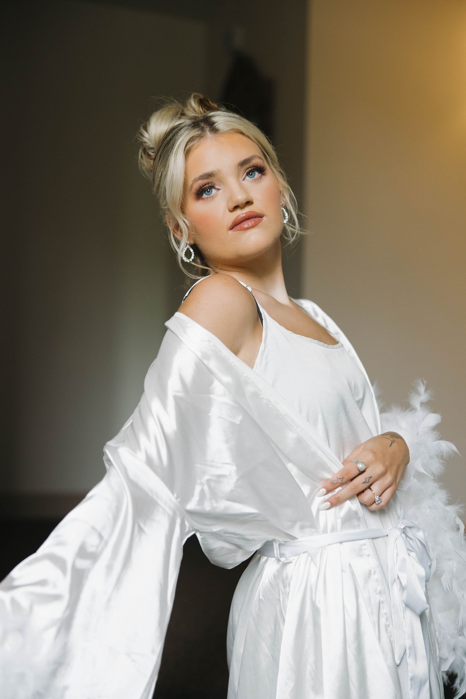 A figure in a flowing white silk robe poses expressively against a warm neutral background.