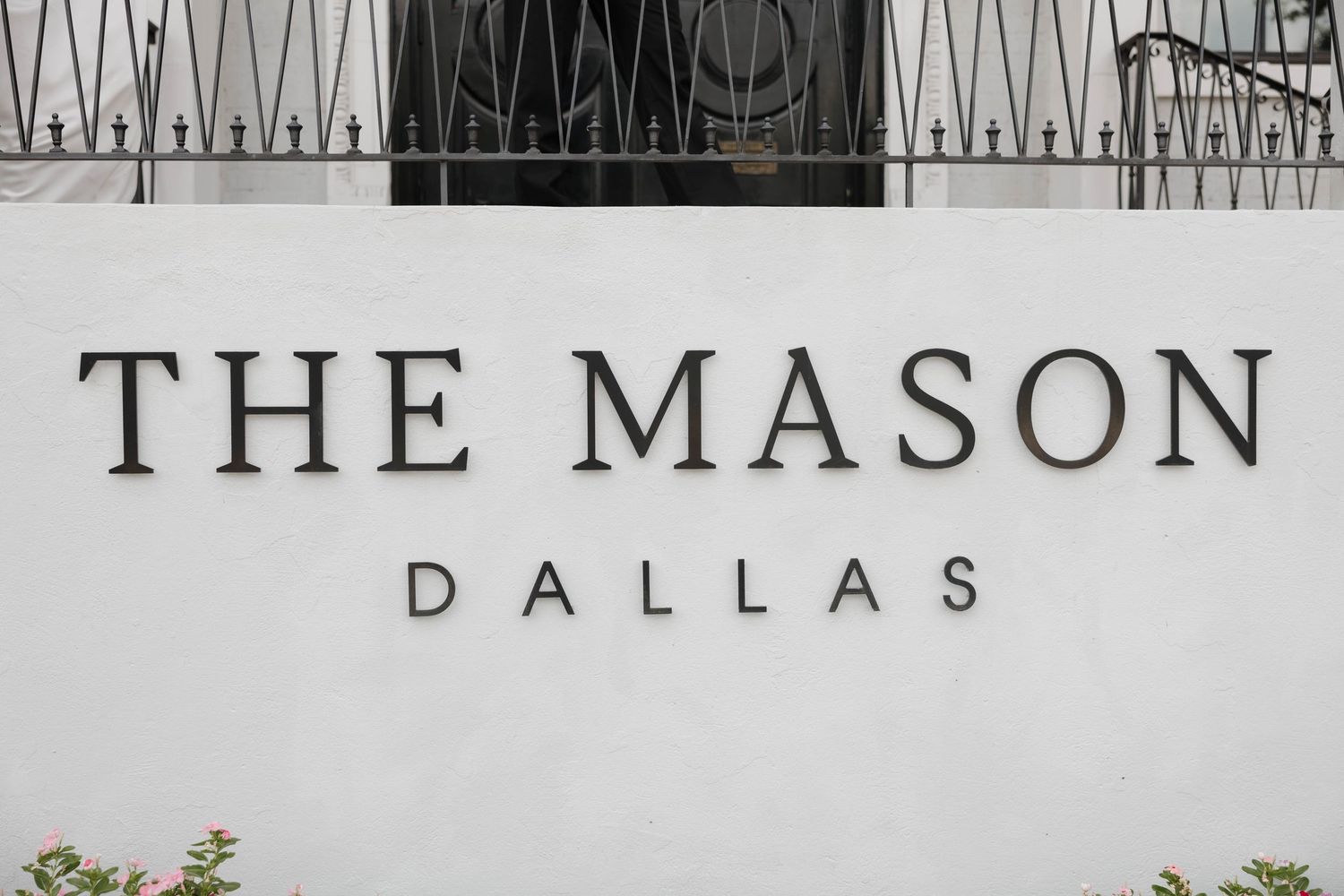 A sign displaying 'THE MASON DALLAS' text with a decorative iron railing mounted above on a white wall.