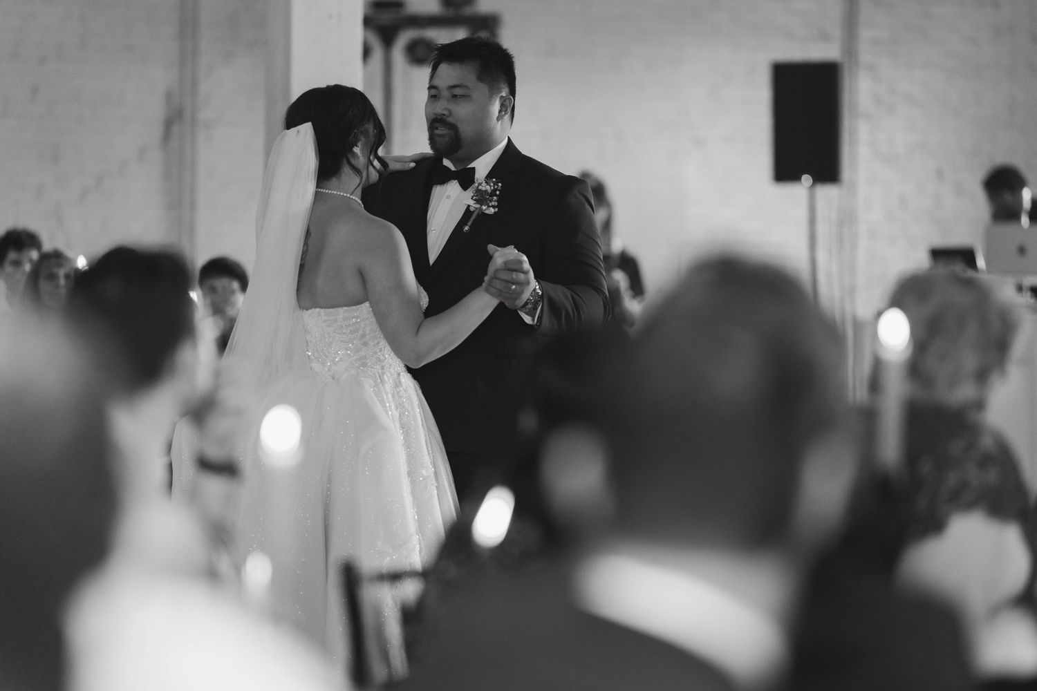 Couple celebrates their emotional first dance at their wedding reception with guests watching from the background.