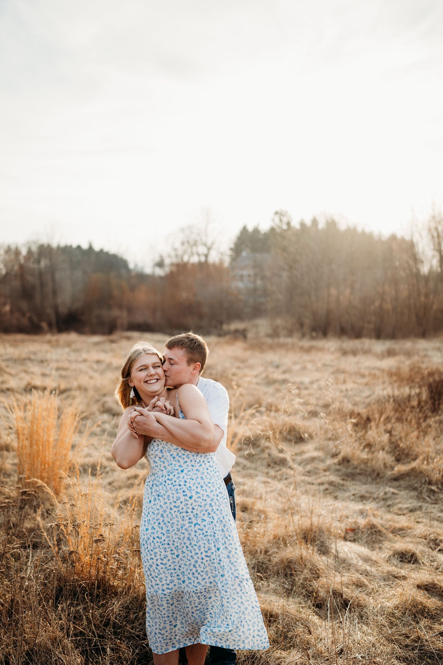 Couple embracing in golden field during sunset with rustic natural backdrop.