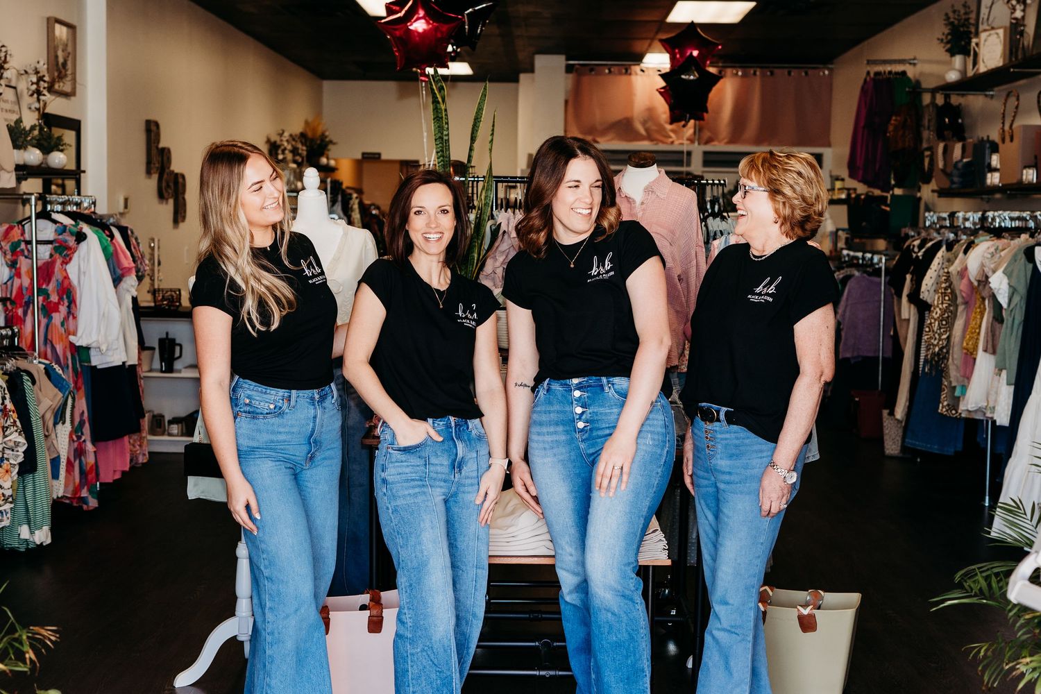 A group wearing matching black t-shirts and blue jeans pose together in a retail clothing store setting.