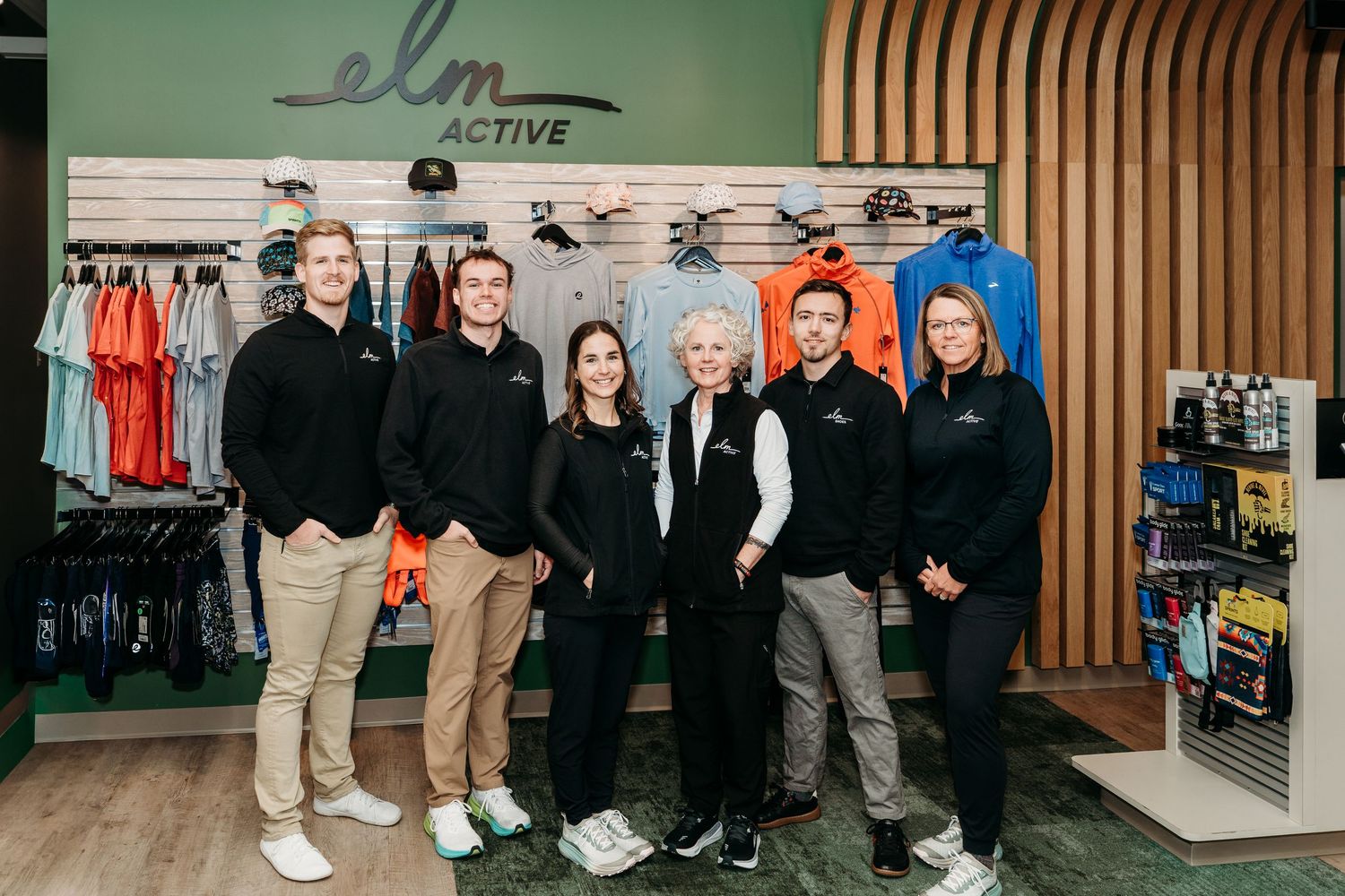 A group of people stand together in a retail store environment with wood paneled walls and clothing displays.