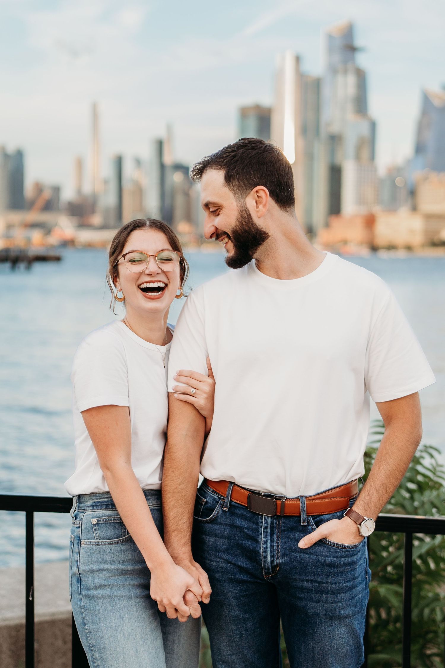 A couple shares a joyful moment together along the waterfront with a city skyline in the background.