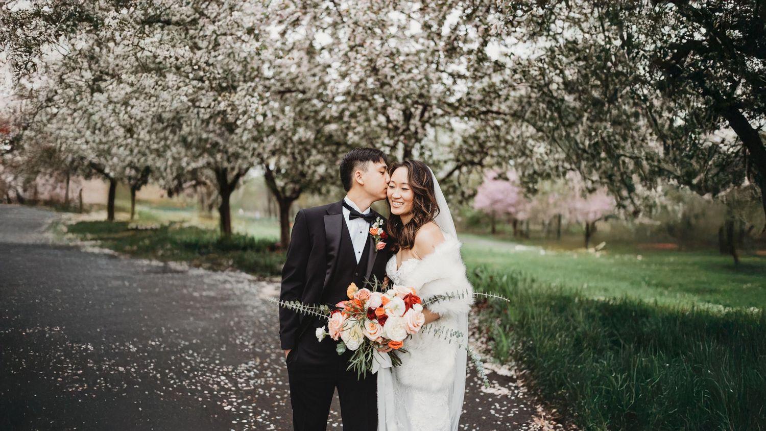 Couple embraces under blooming cherry blossom trees on a spring day as petals float through the air.