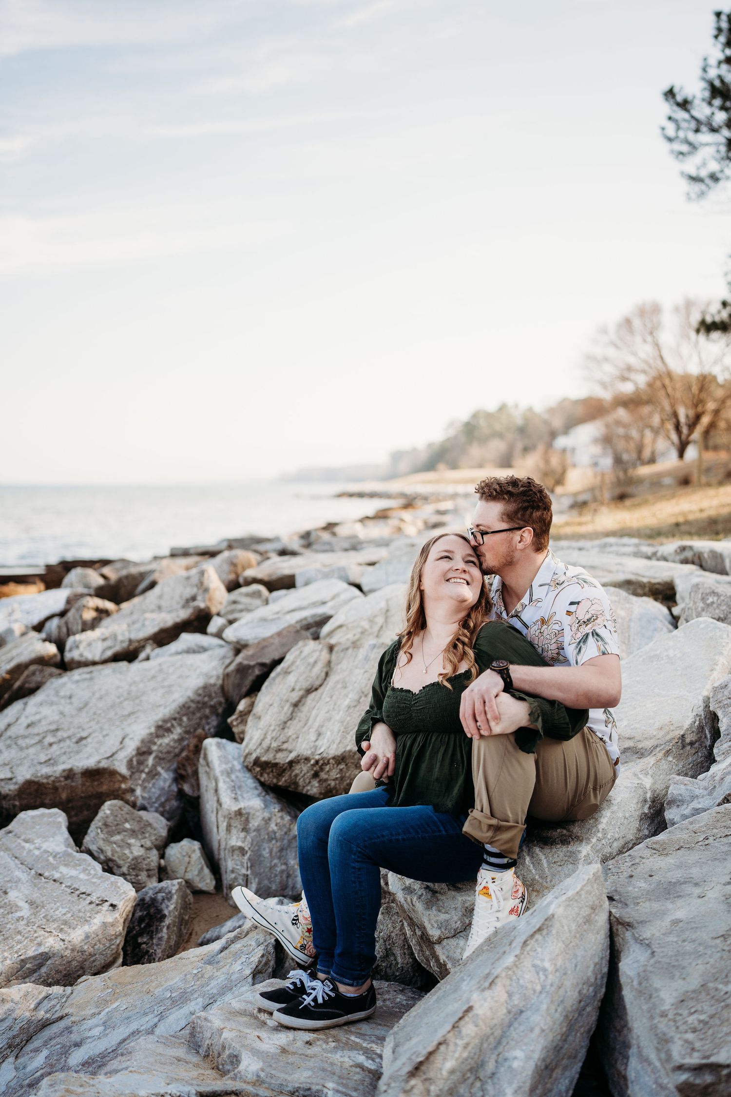 Couple sharing intimate moment while sitting on rocky coastline during sunset.