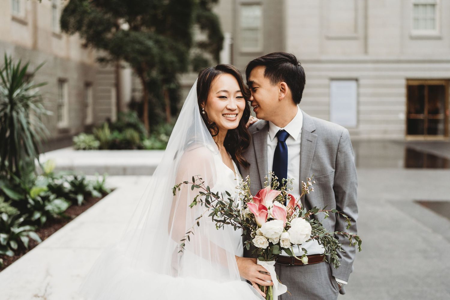 Happy newlyweds share a joyful moment together outdoors with a beautiful wedding bouquet.