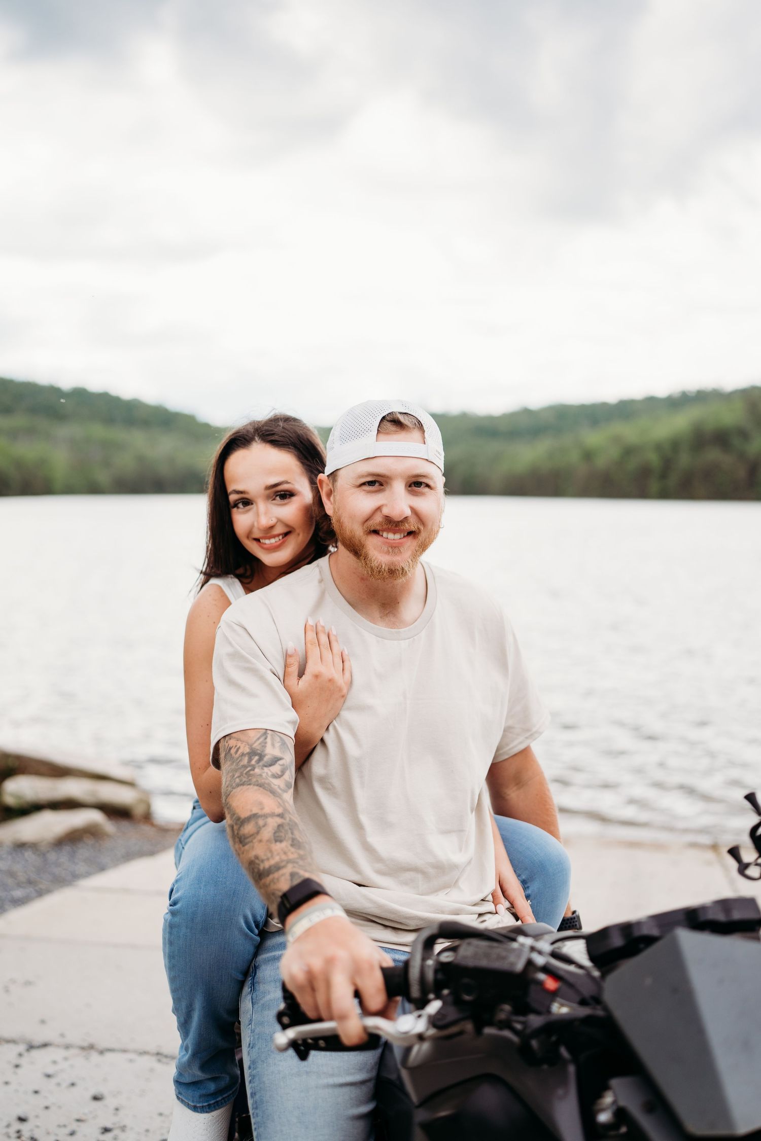 Couple sitting together on ATV by scenic lake surrounded by hills.