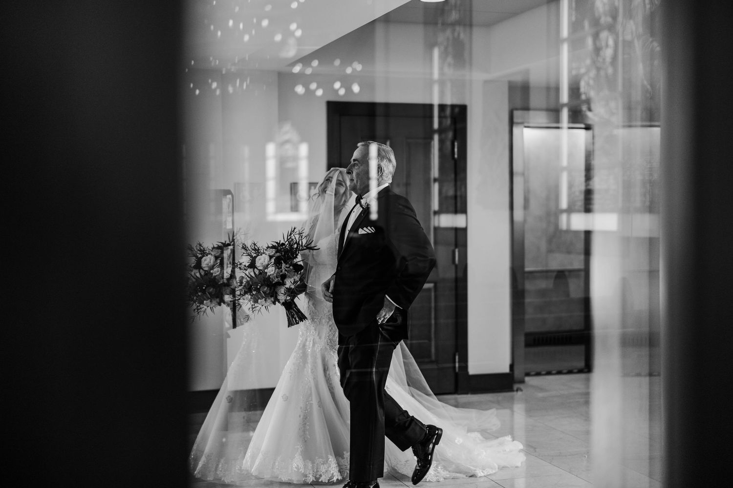 Black and white photograph of a bride and groom kissing in a romantically lit venue entrance.