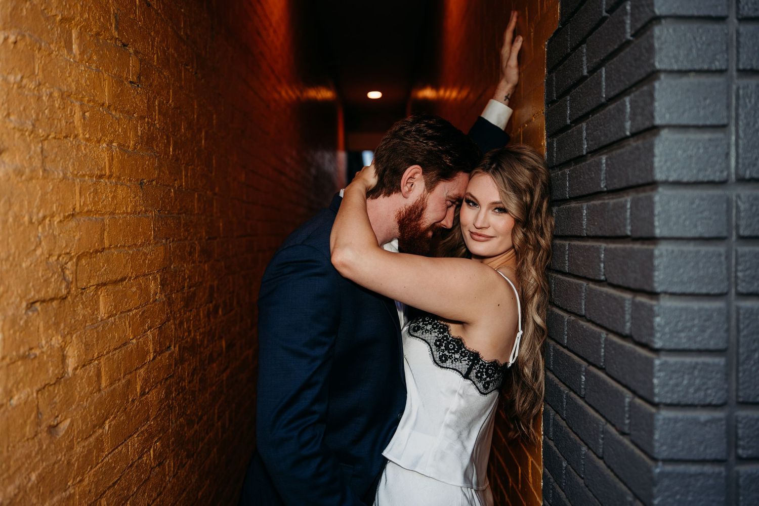 Romantic wedding couple embraces in an intimate moment between brick walls during their wedding photoshoot.