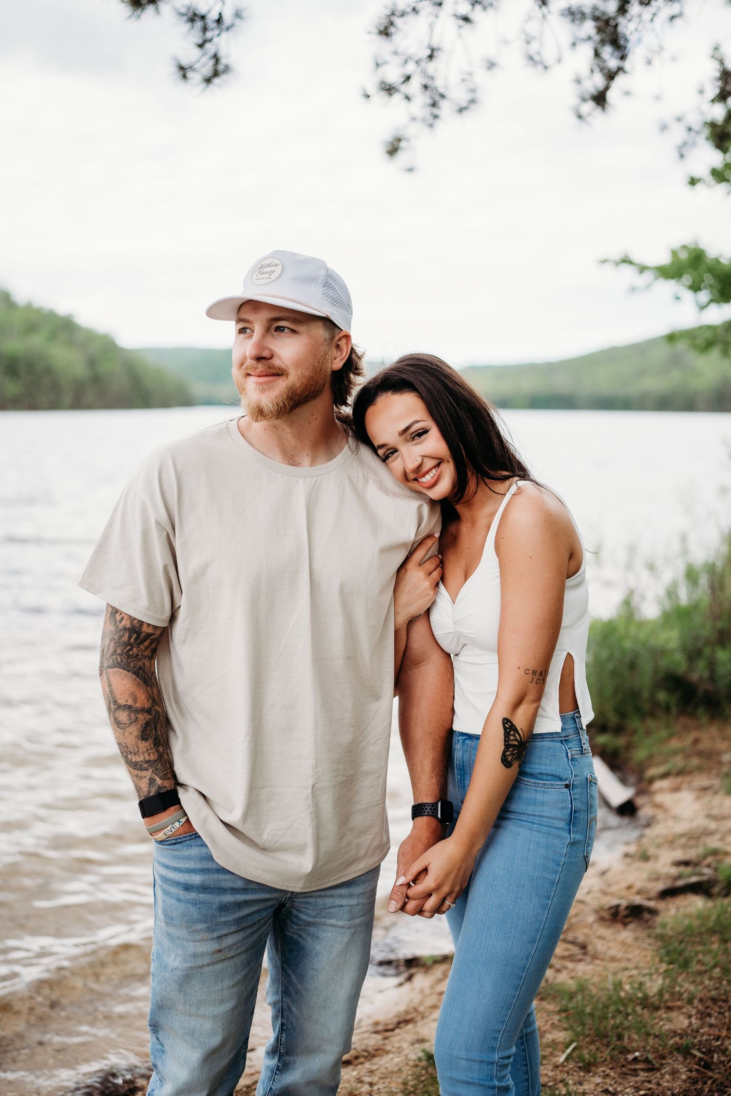 A casual couple posing together by a serene lake on a sunny day.