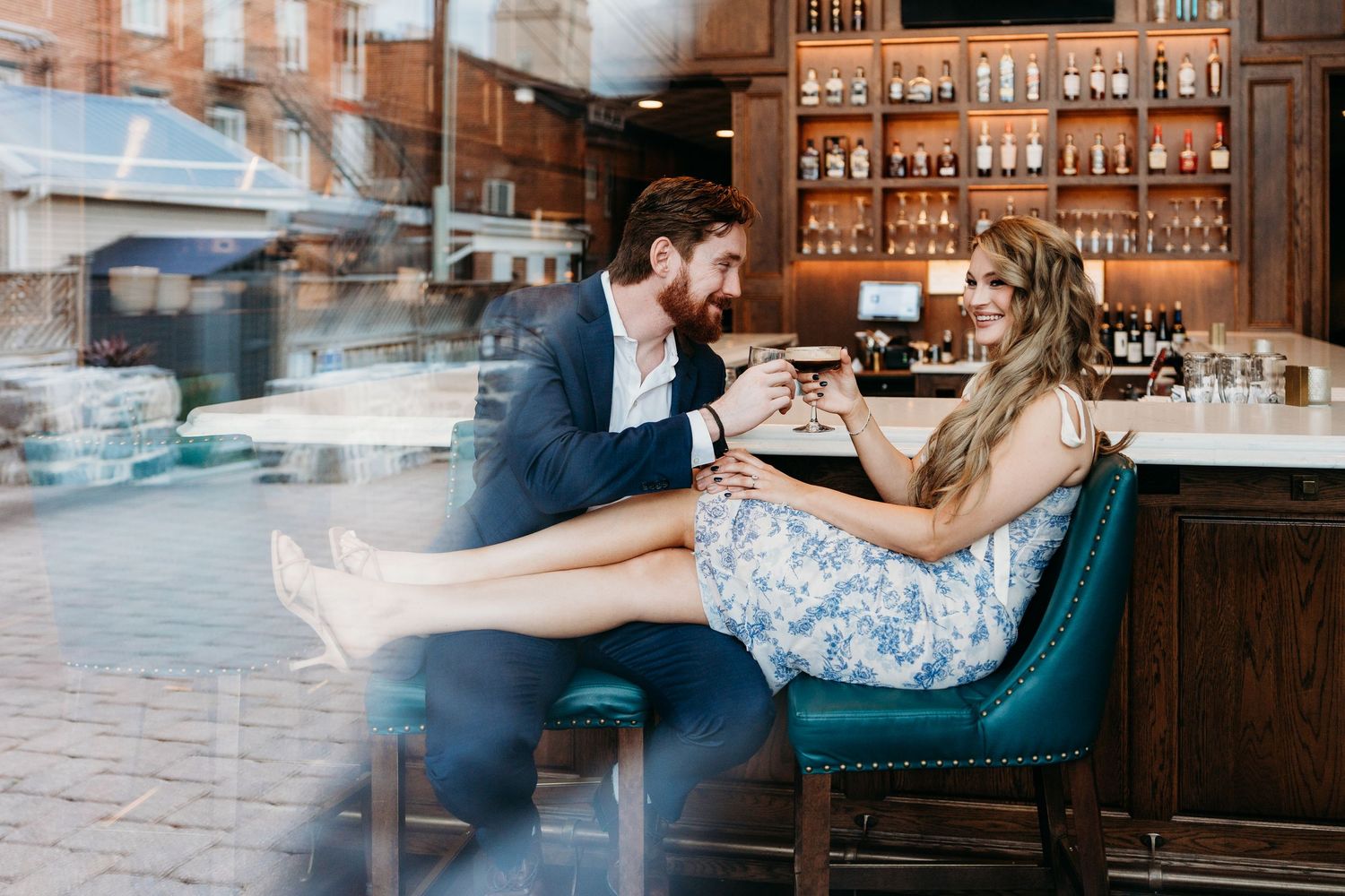 Romantic couple shares tender moments in an elegant bar setting with teal velvet seating and ambient lighting.