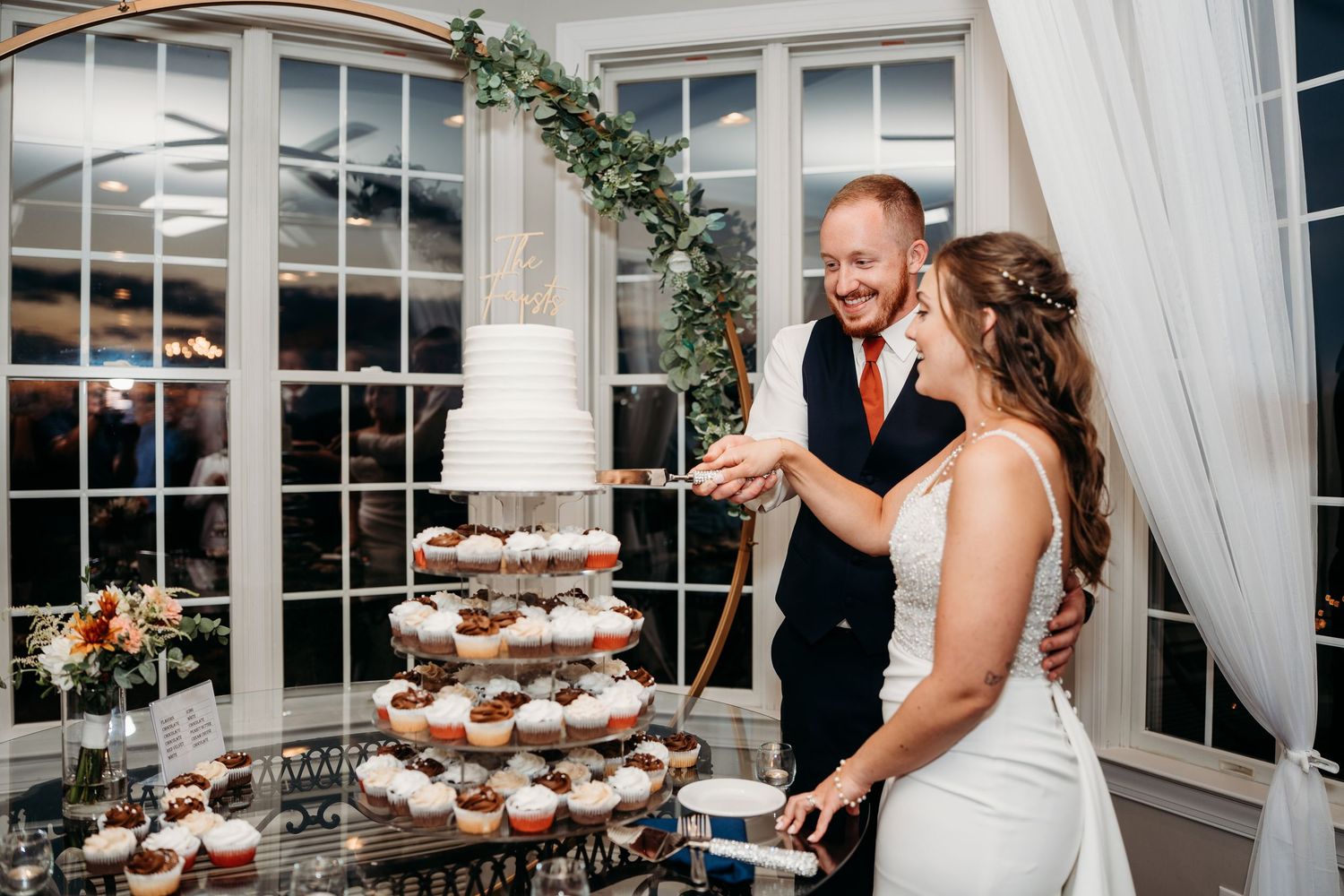 Wedding couple cuts their white tiered cake together during elegant reception celebration.