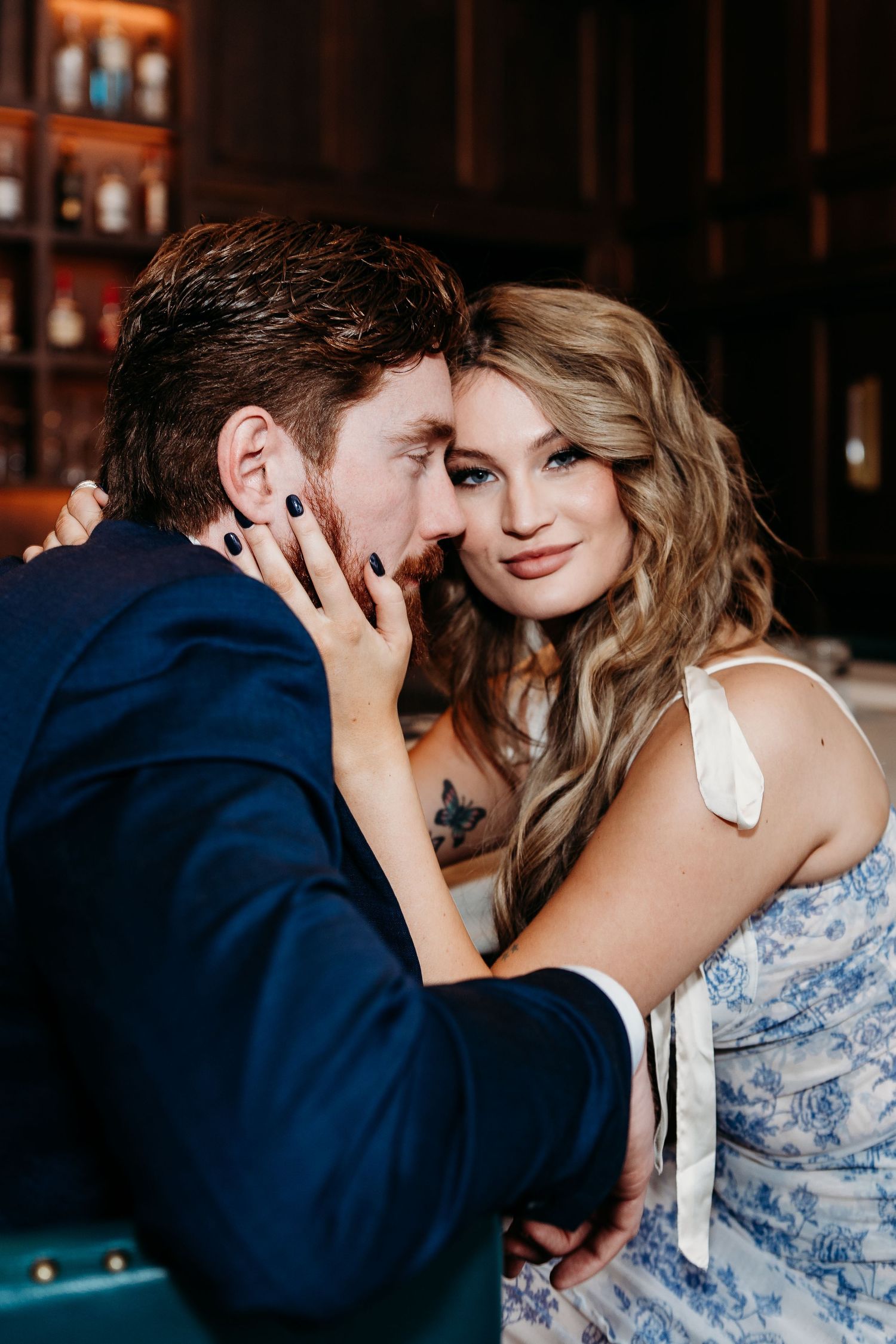 A romantic couple in formal attire share an intimate moment at a dimly lit bar.
