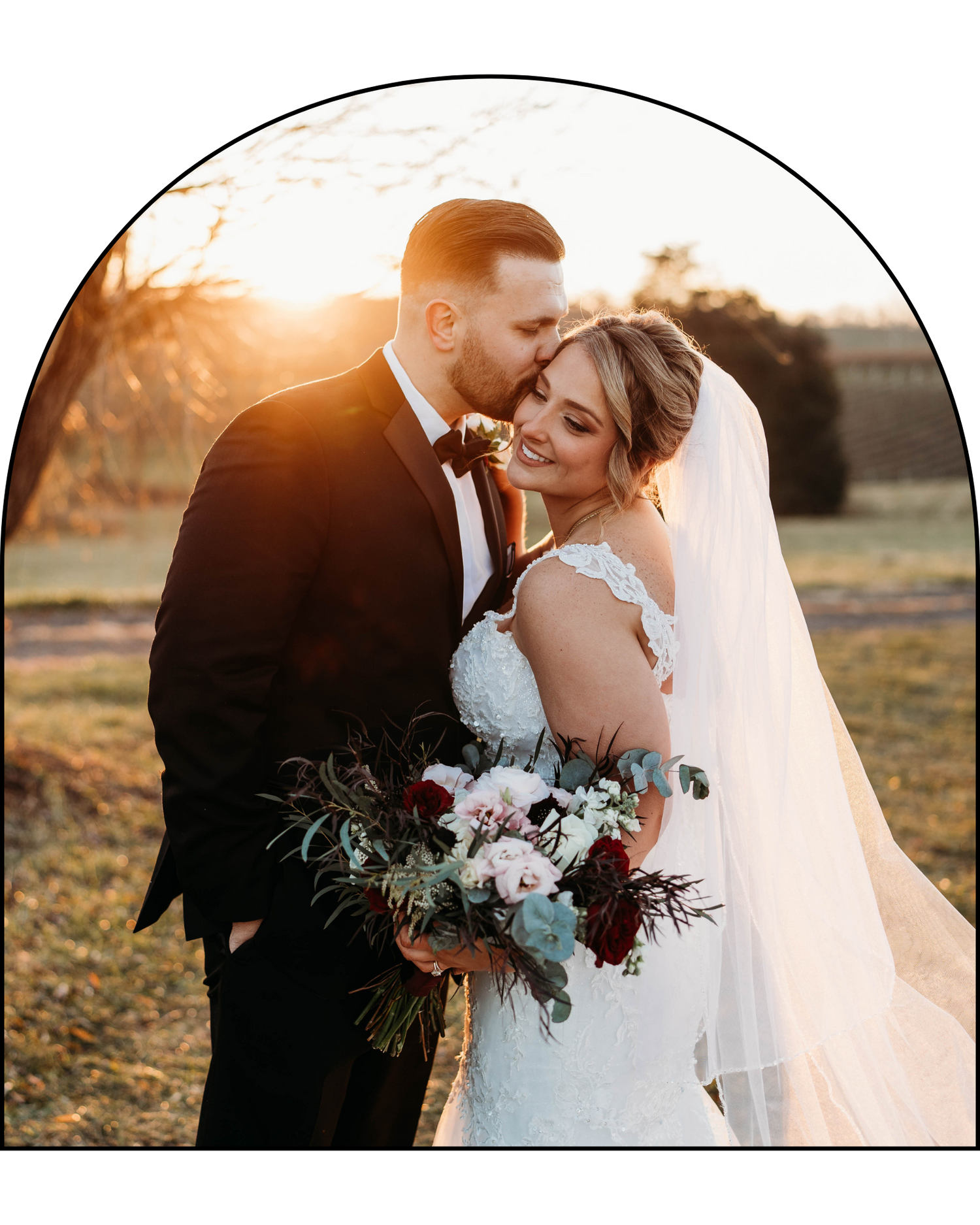 A romantic sunset wedding portrait with a bouquet of blush and burgundy flowers against golden light.