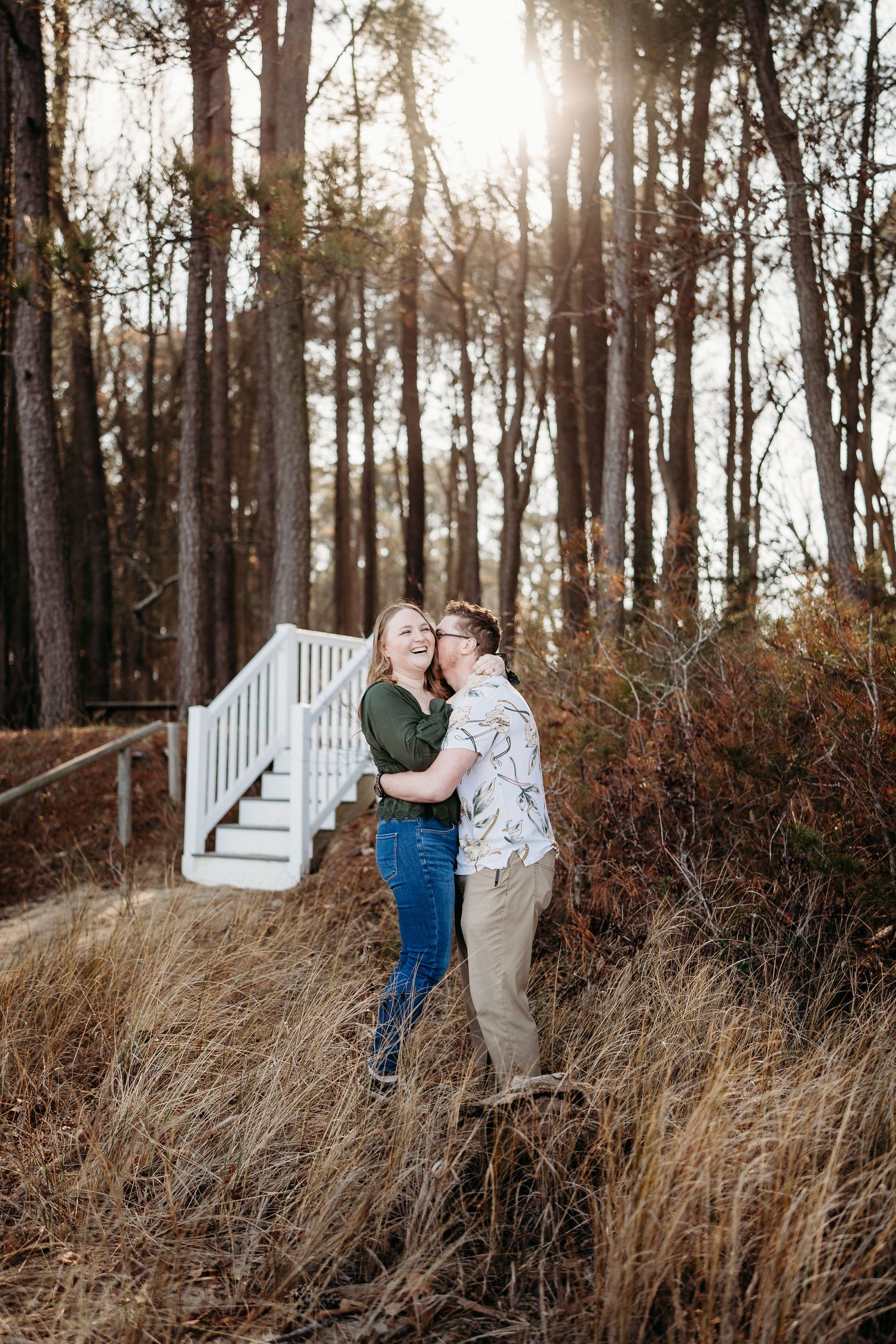 Couple embracing on hillside with white stairs and autumn forest backdrop.