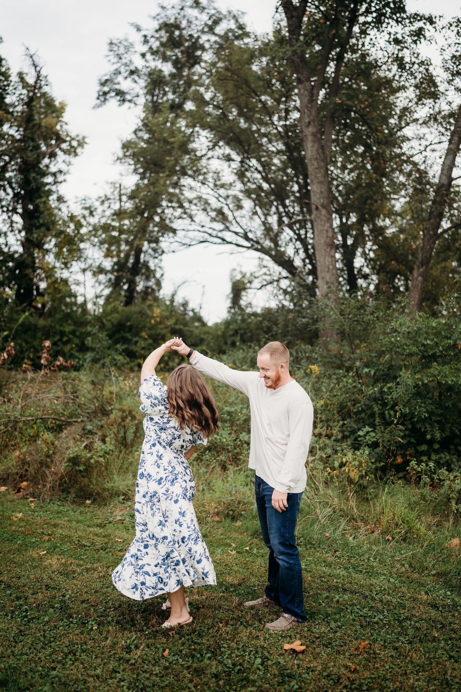 Couple dancing playfully in garden setting with natural greenery backdrop.