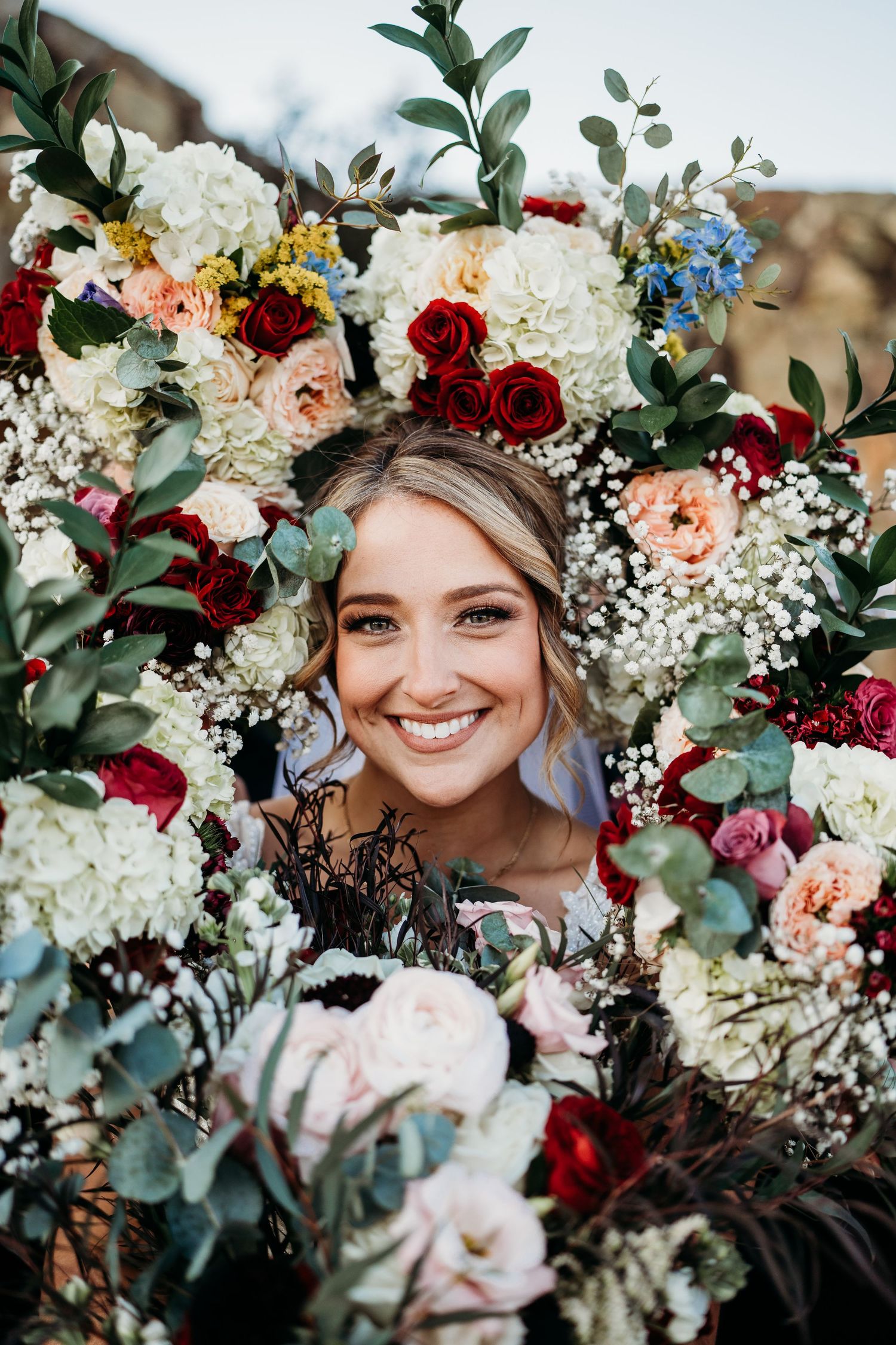 A colorful bridal bouquet featuring red roses, white hydrangeas, baby's breath and greenery creates a stunning floral frame.