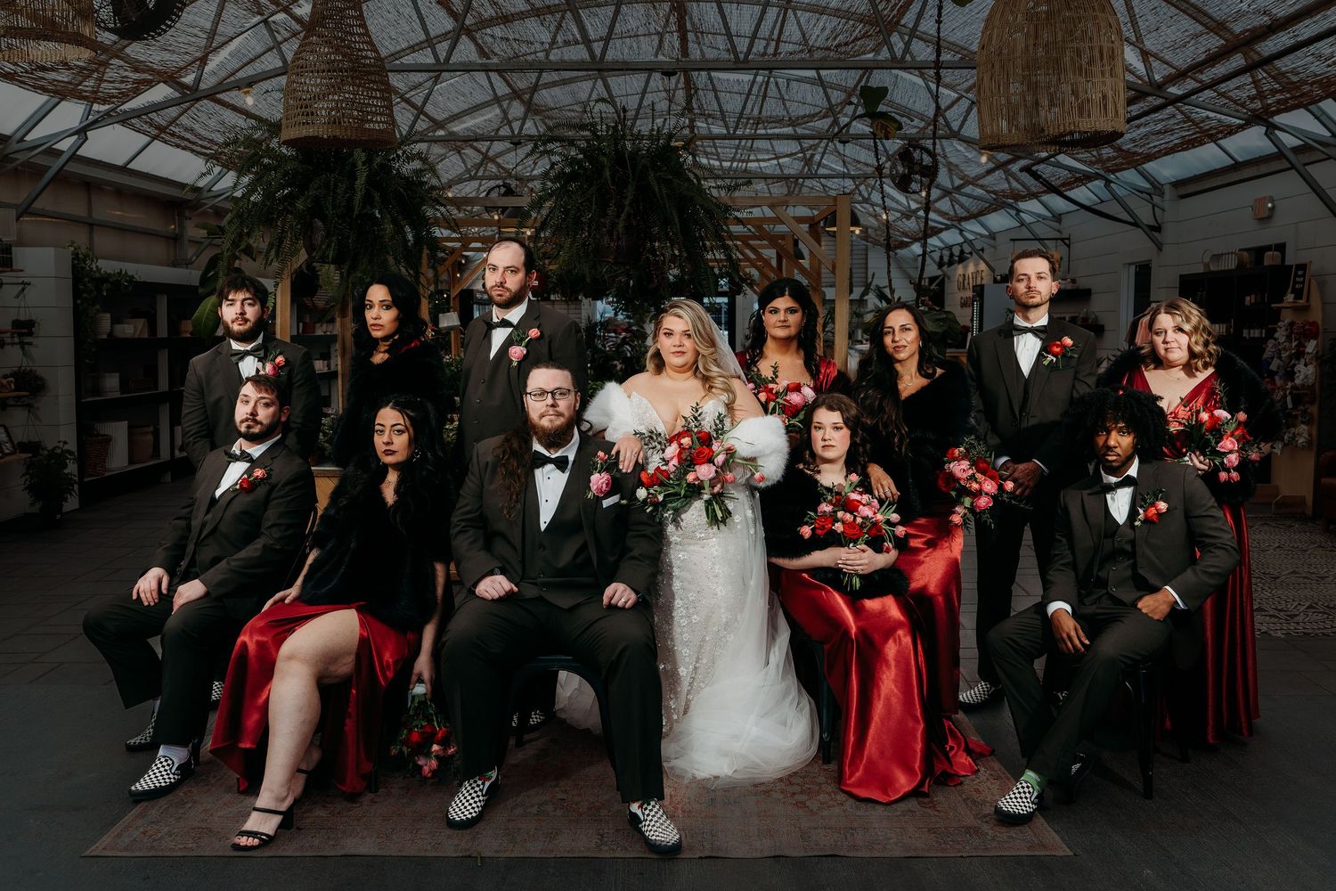 Wedding party poses together on bench in greenhouse with elegant red and black attire.