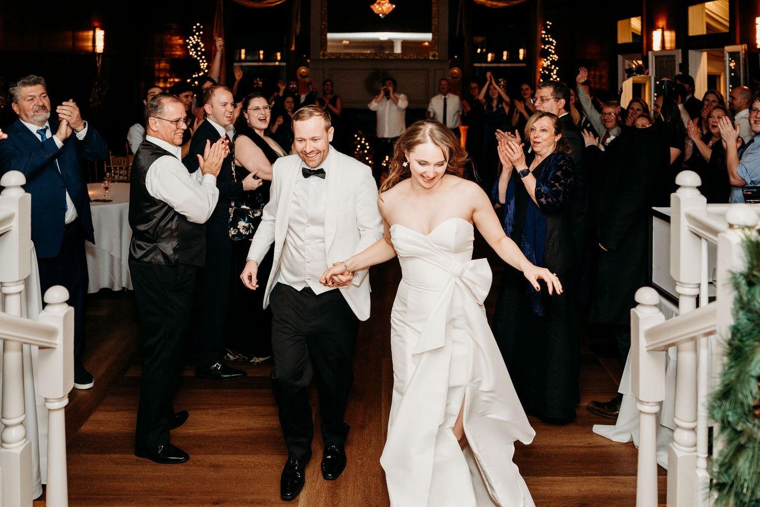 A couple joyfully exits their wedding ceremony while guests cheer in a dimly lit venue with candlelight.