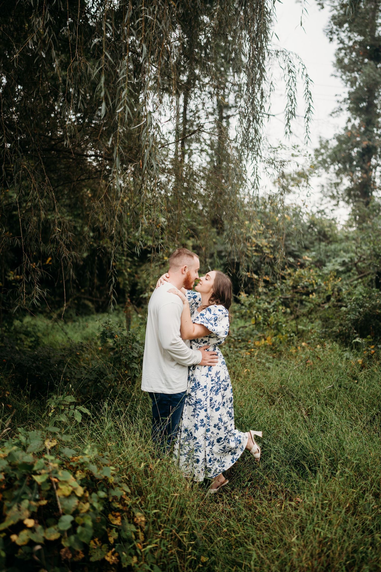 A couple sharing an intimate moment under weeping willow trees in a lush garden setting.