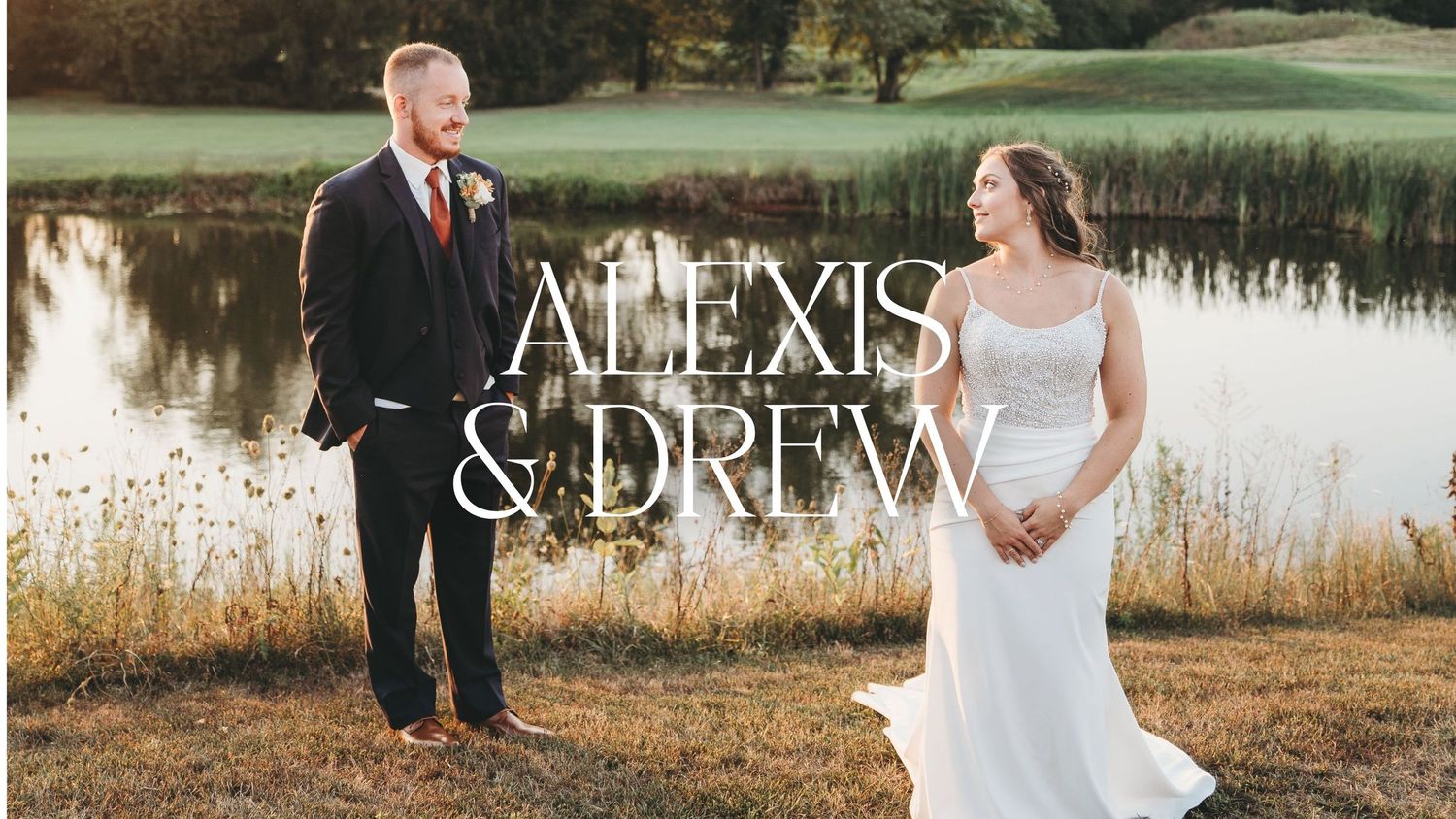 Alexis and Drew wedding photo with bride in white gown and groom in navy suit standing by a pond in a field.
