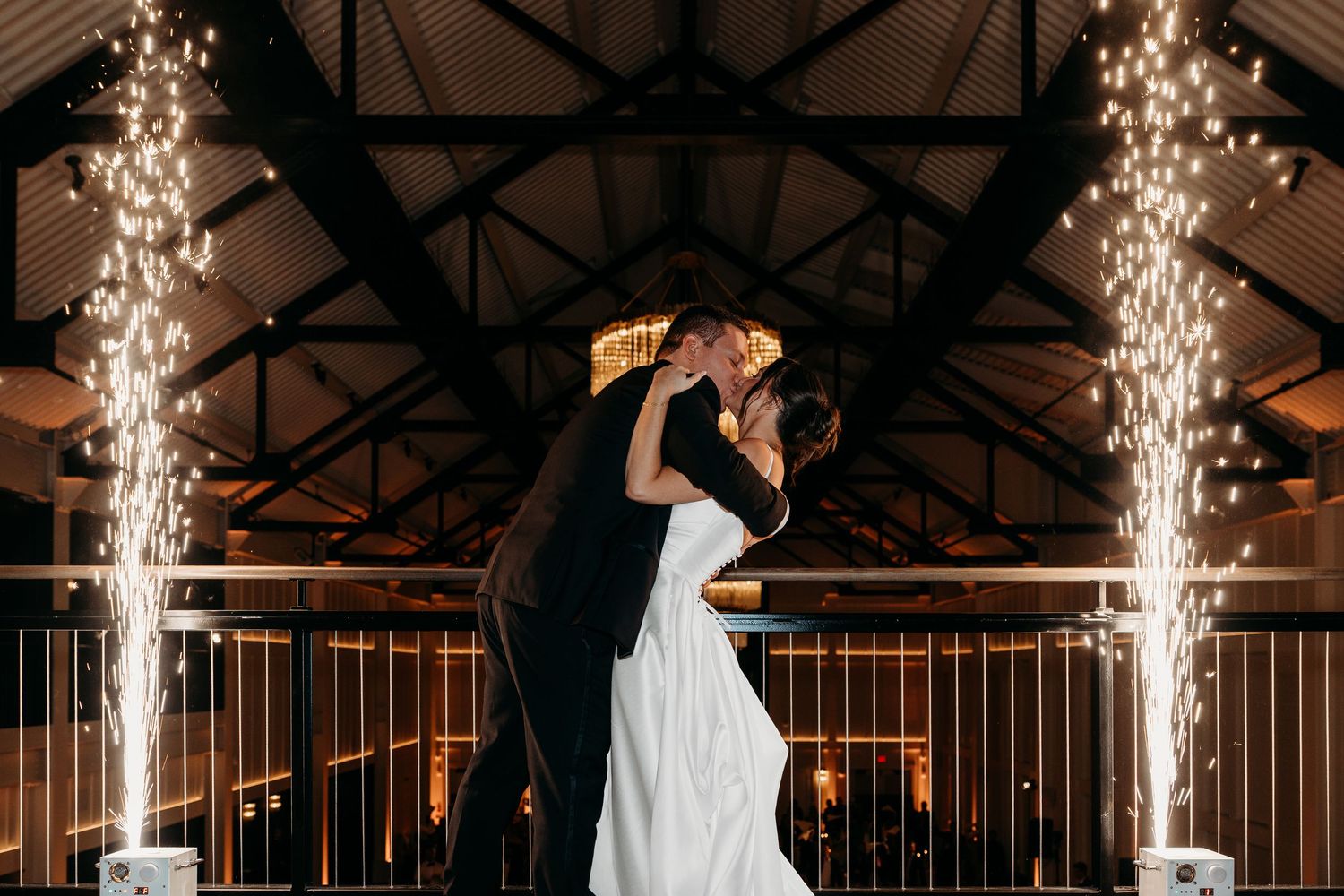 Wedding couple dances under dramatic indoor sparkler fountains creating magical lighting effects on a dark dance floor.