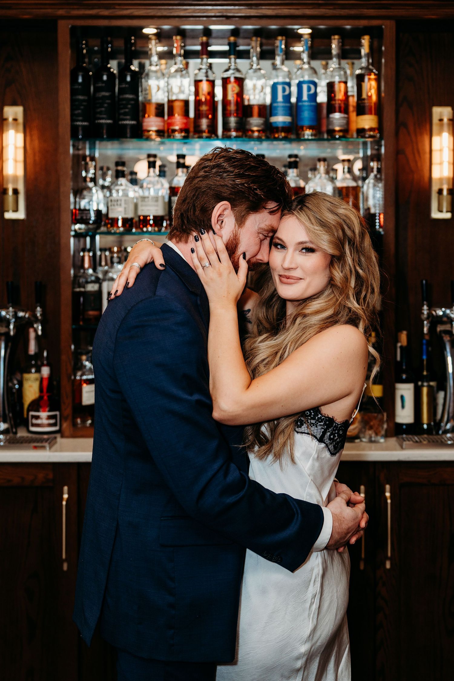 A couple shares an intimate dance moment at a bar with bottles and warm lighting in the background.