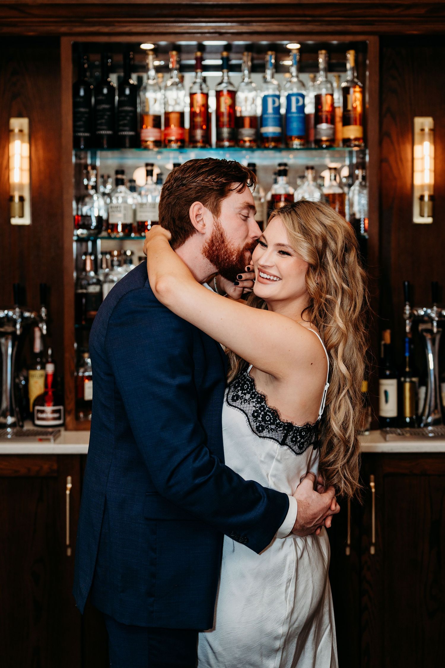 A romantic moment between a couple dancing and embracing at a bar with bottles in the background.