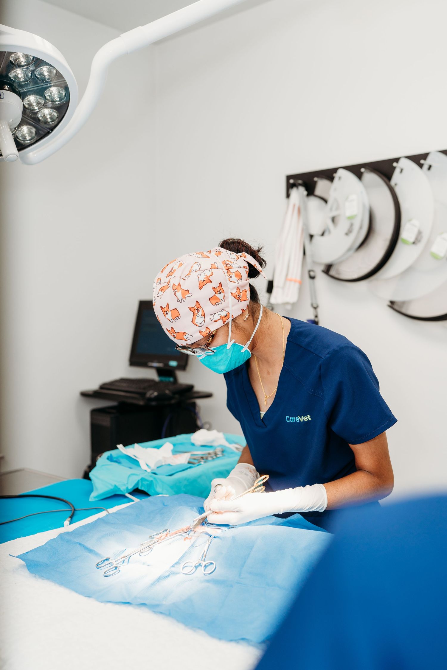 Medical professional in surgical scrubs and cap performing detailed work on a blue surgical table in a clinical setting.